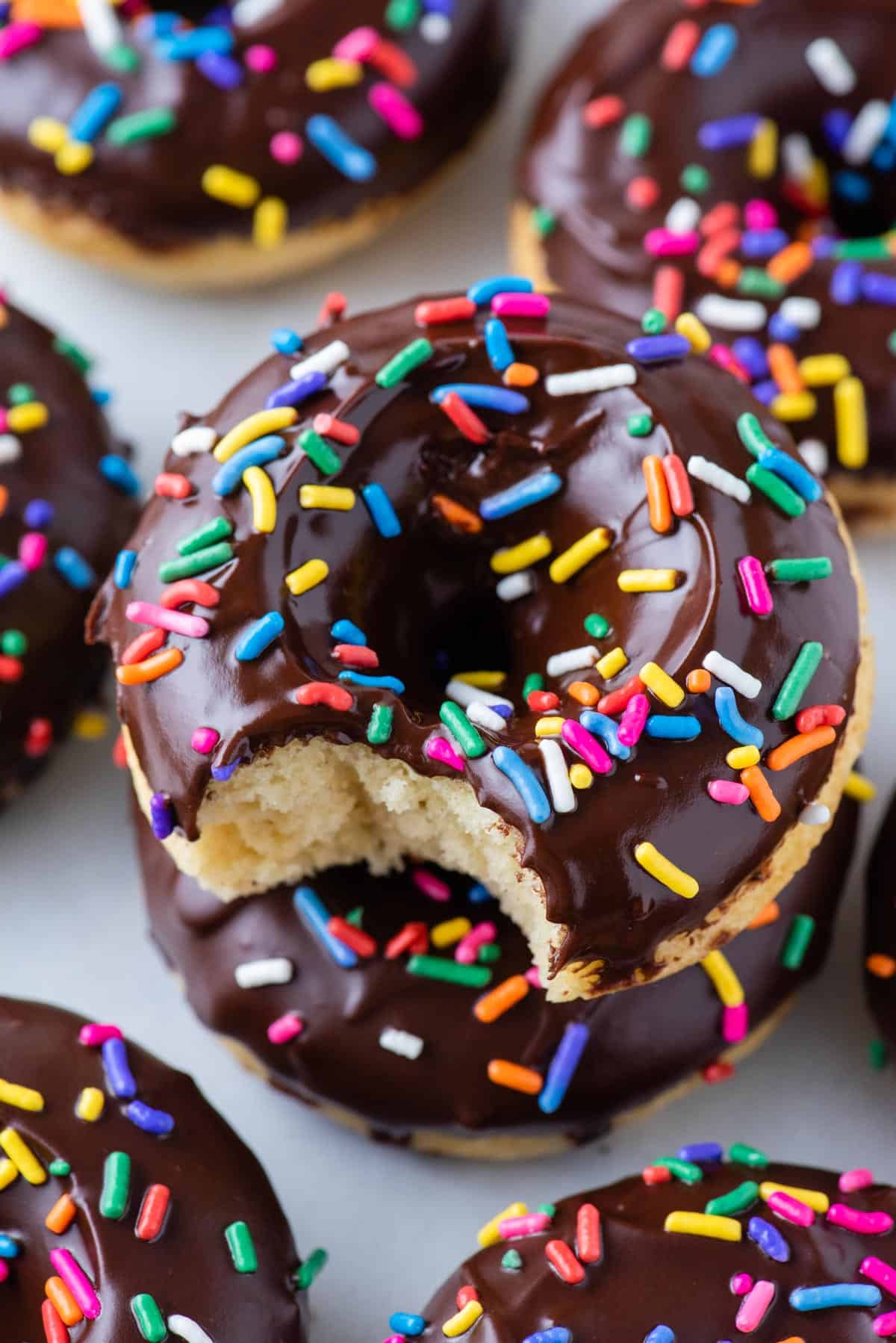 close up of a donut topped with chocolate glaze and sprinkles with more donuts in the background
