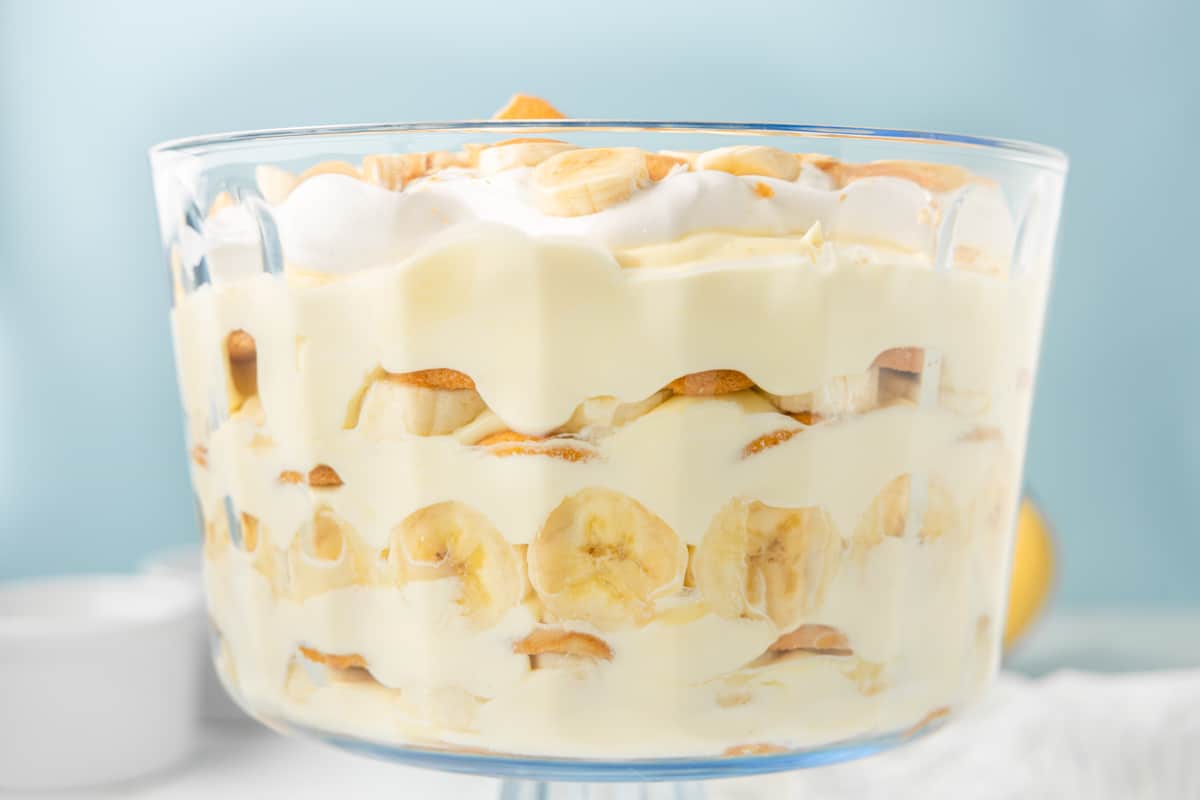 Close up of the side of a trifle dish with banana pudding layered inside of it against a blue background