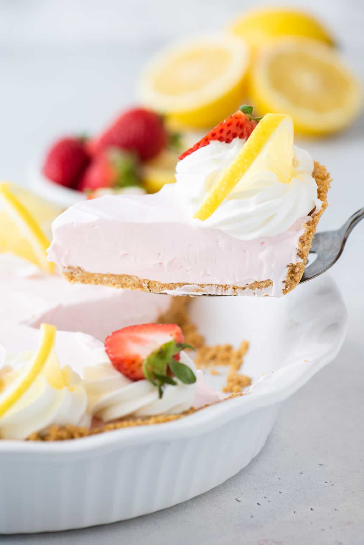 a slice of kool aid pie topped with lemon and strawberry being lifted out of a white pie dish with a spatula