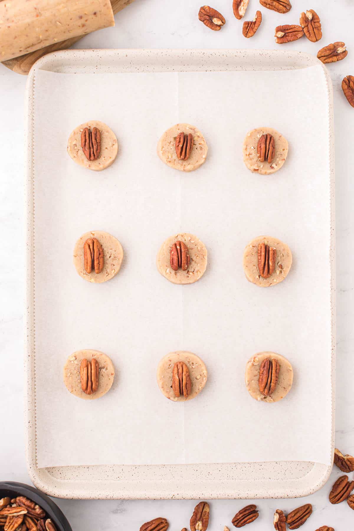 pecan sandie cookies in rows on a baking sheet lined with parchment paper surrounded by pecans