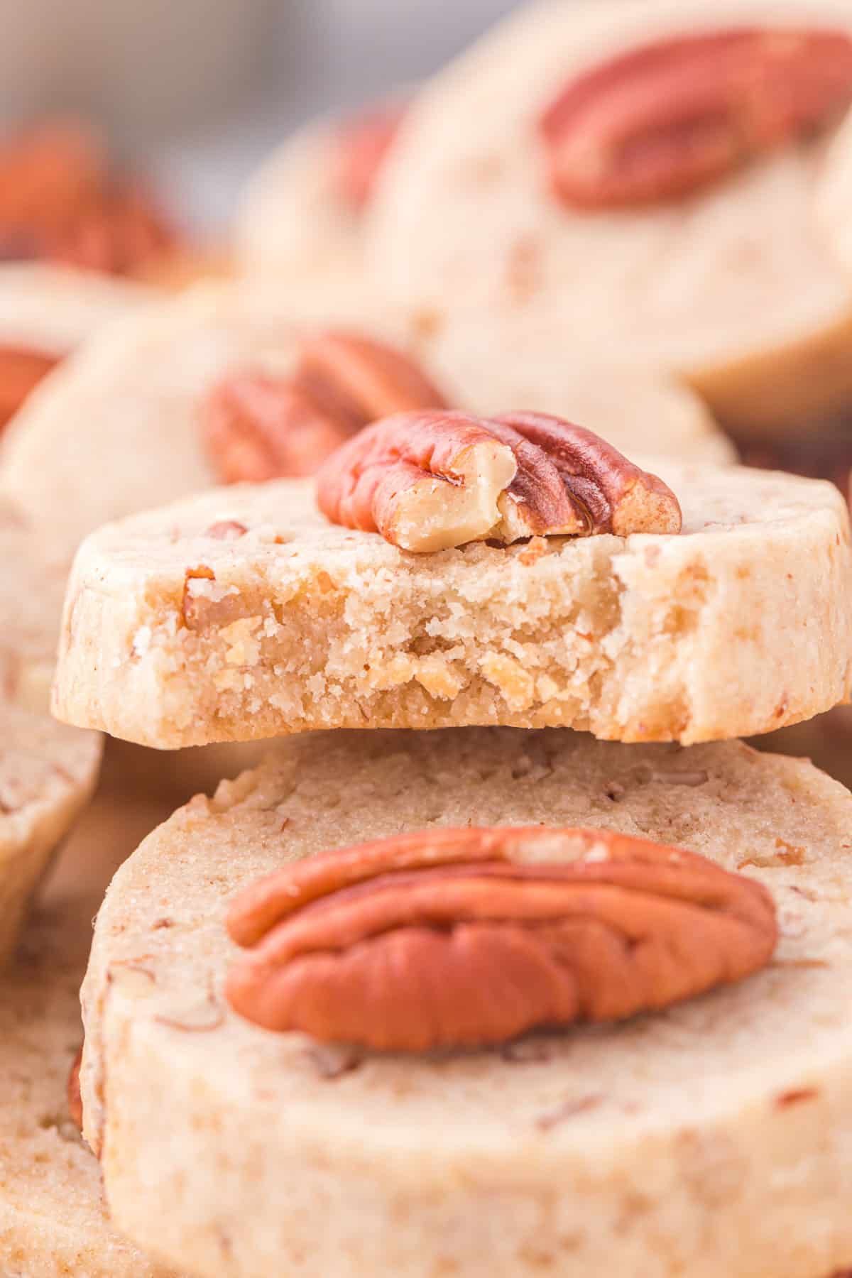 a pile of pecan sandies with one cookie on top that has a bite out of it