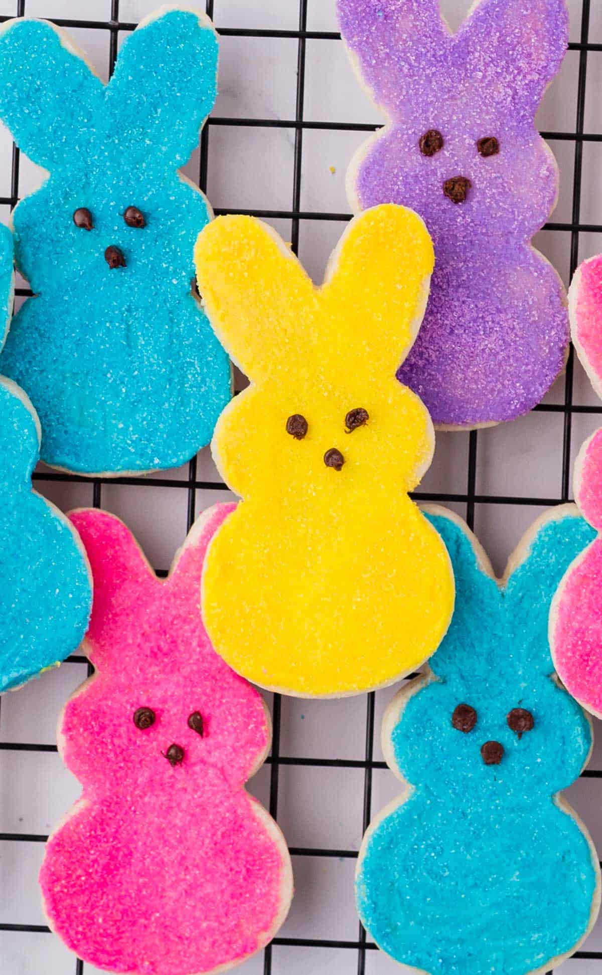 blue, pink, purple and yellow peeps bunny cookies stacked up on a cooling rack
