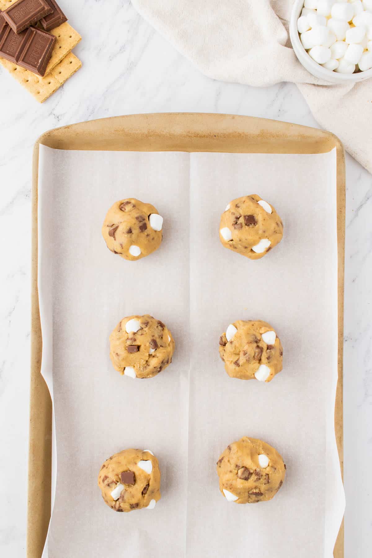 smores cookie dough balls lined on a parchment paper on a baking sheet