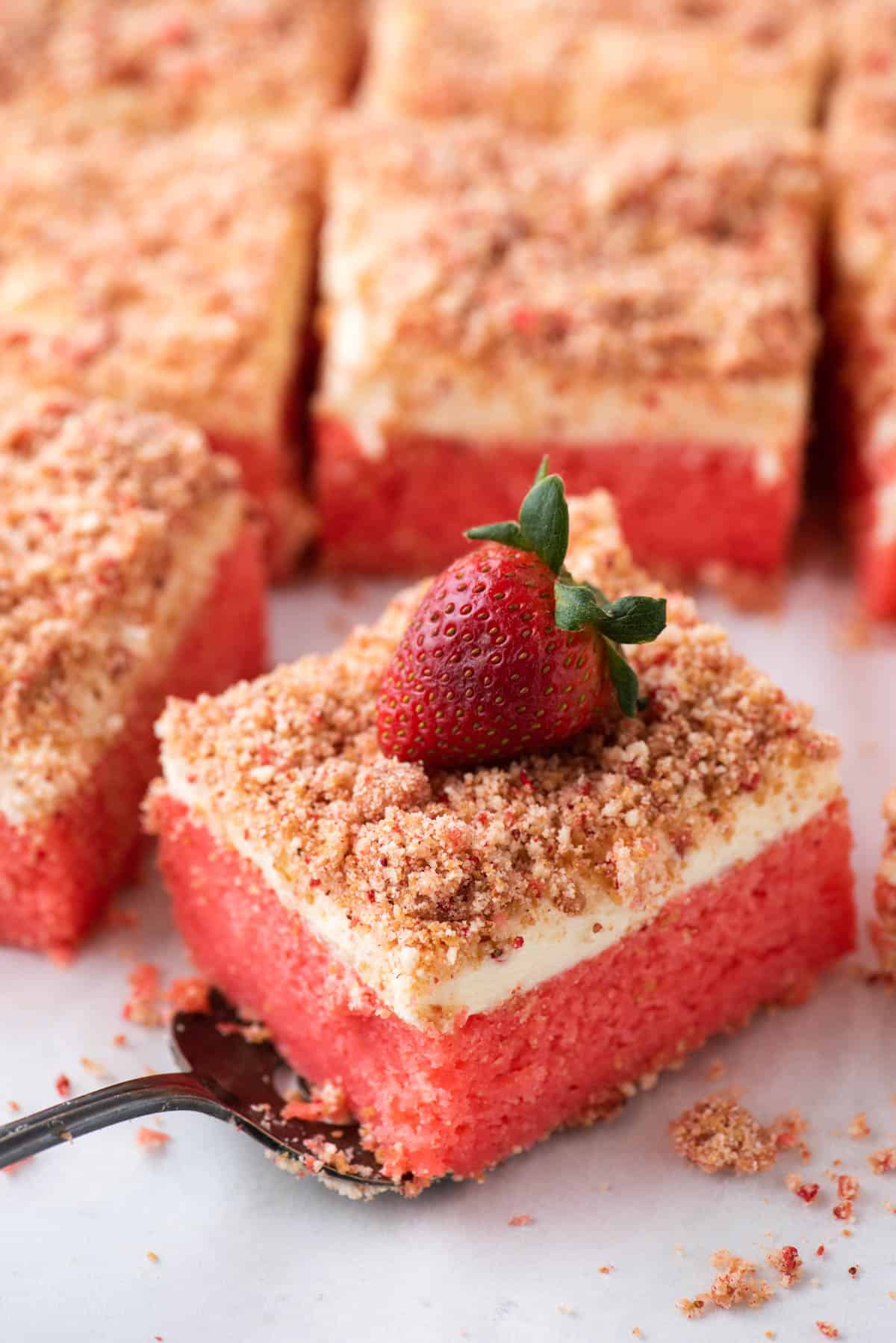 a slice of strawberry crunch cake on a spatula with more slices of cake in the background