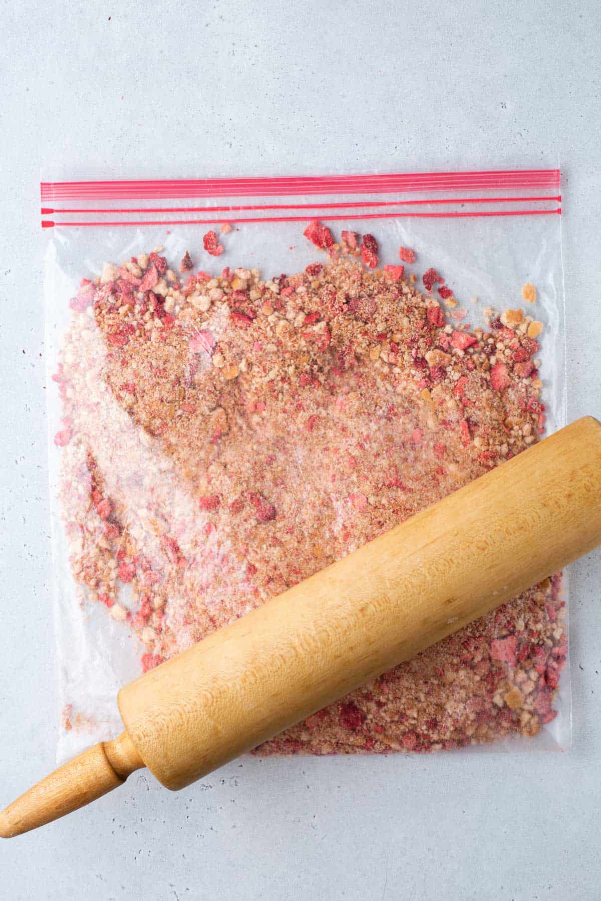 crushed nilla wafers and freeze dried strawberries in a ziploc bag with a rolling pin on top of it