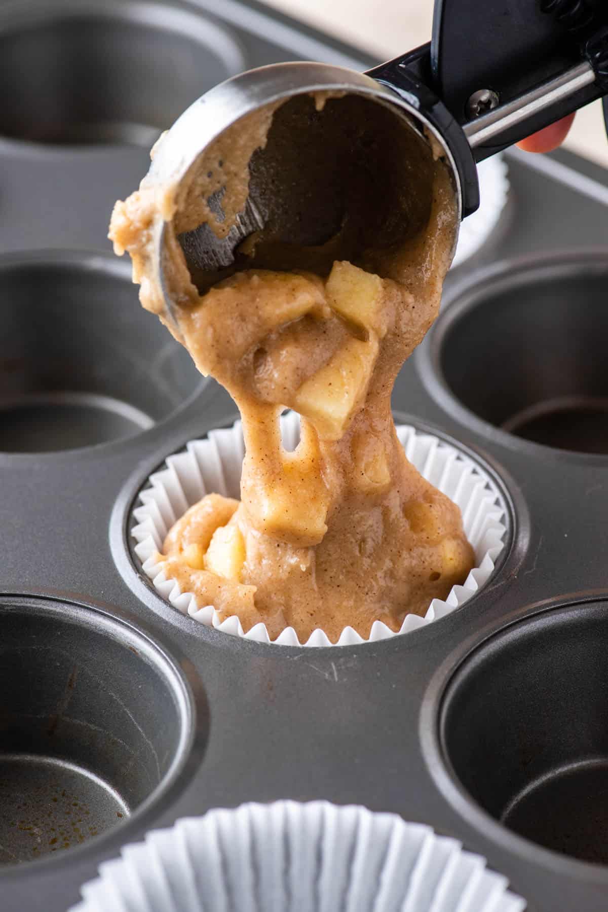 apple cinnamon muffins batter being scooped into a muffin liner inside a muffin pan