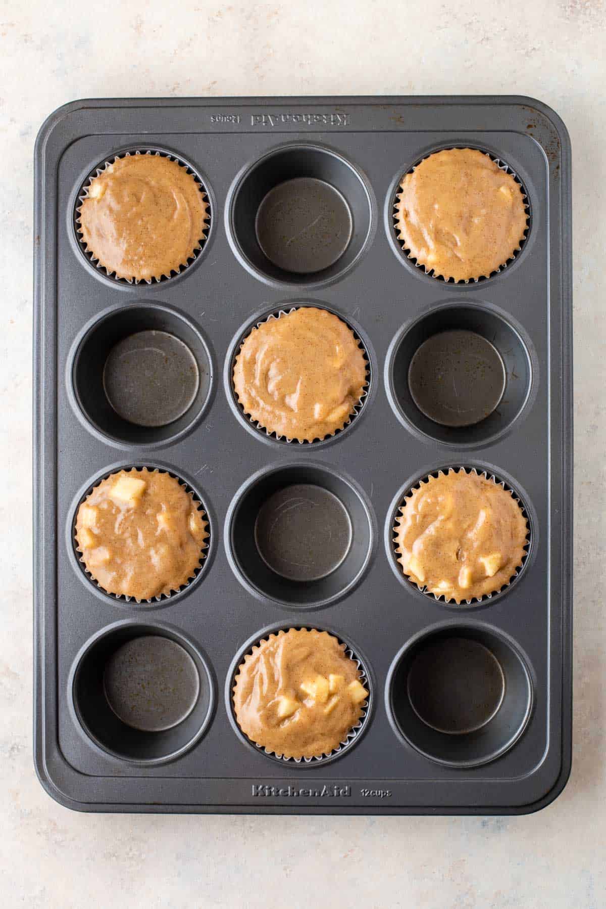 a muffin pan with apple cinnamon muffin batter in every other muffin hole
