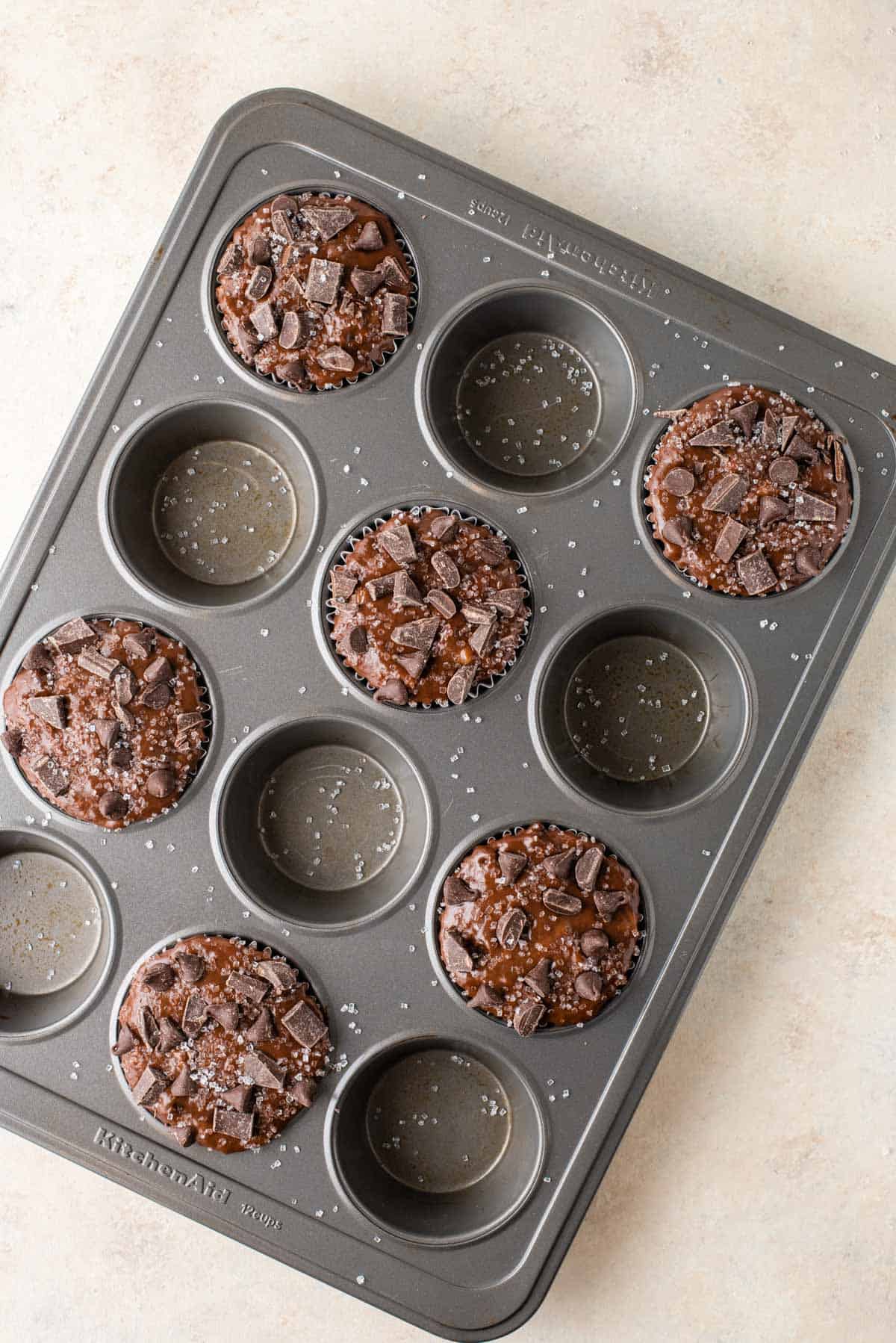 a muffin pan with chocolate banana muffins in every other muffin hole sprinkled with salt on top