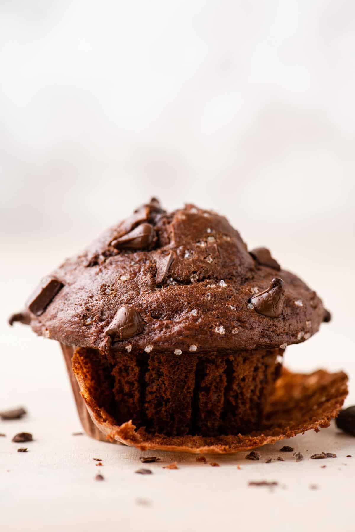 a close up of the side of a chocolate banana muffin with the muffin paper pulled partially off