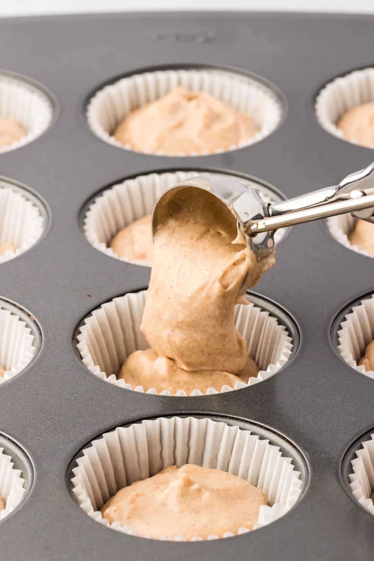 a cookie scooper filling a muffin tin with muffin liners full of churro cupcake batter