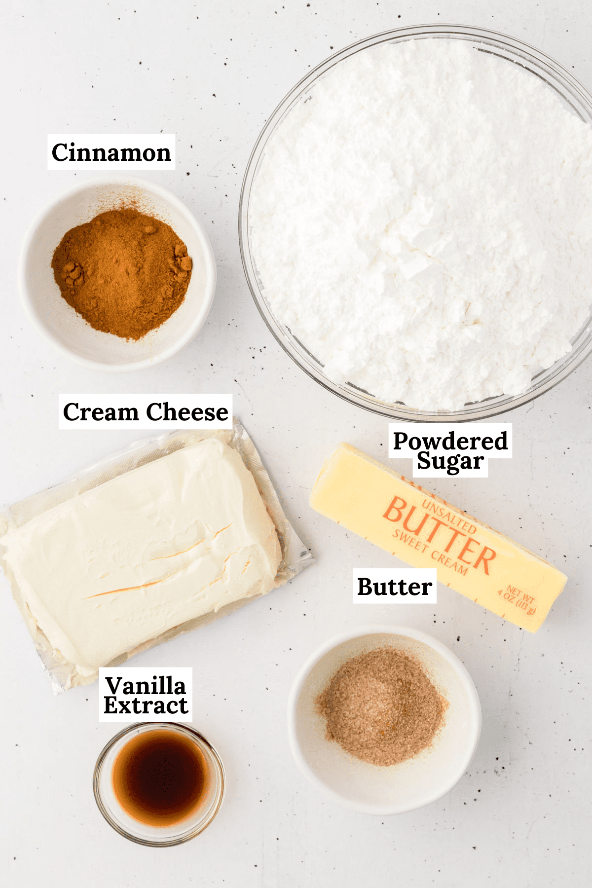 ingredients for cinnamon cream cheese frosting including cinnamon, powdered sugar, cream cheese, butter, vanilla extract and cinnamon sugar