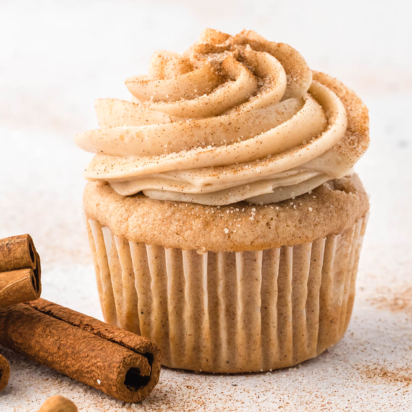 cinnamon cream cheese frosting on top of a cupcake with cinnamon sticks beside it