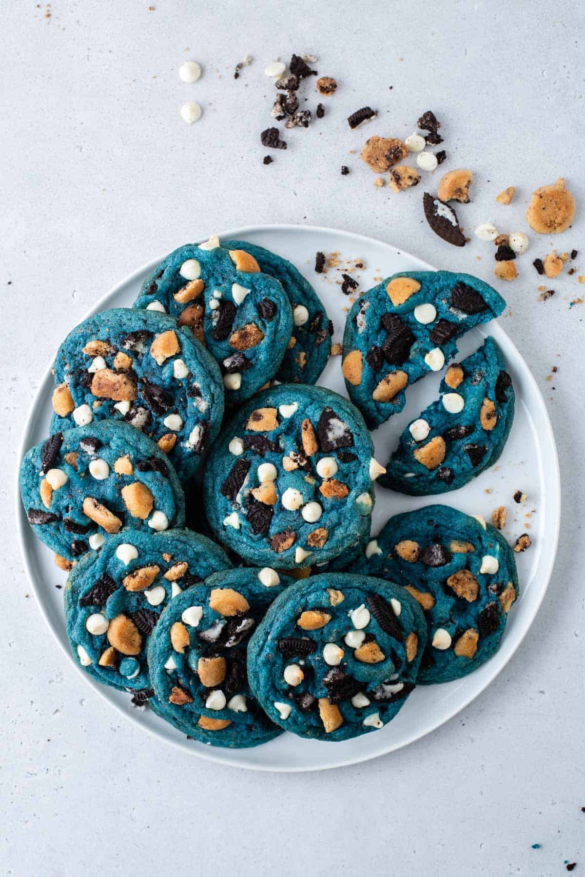 a plate full of cookie monster cookies with one cookie on the right pulled into halves and cookie crumbs sprinkled around
