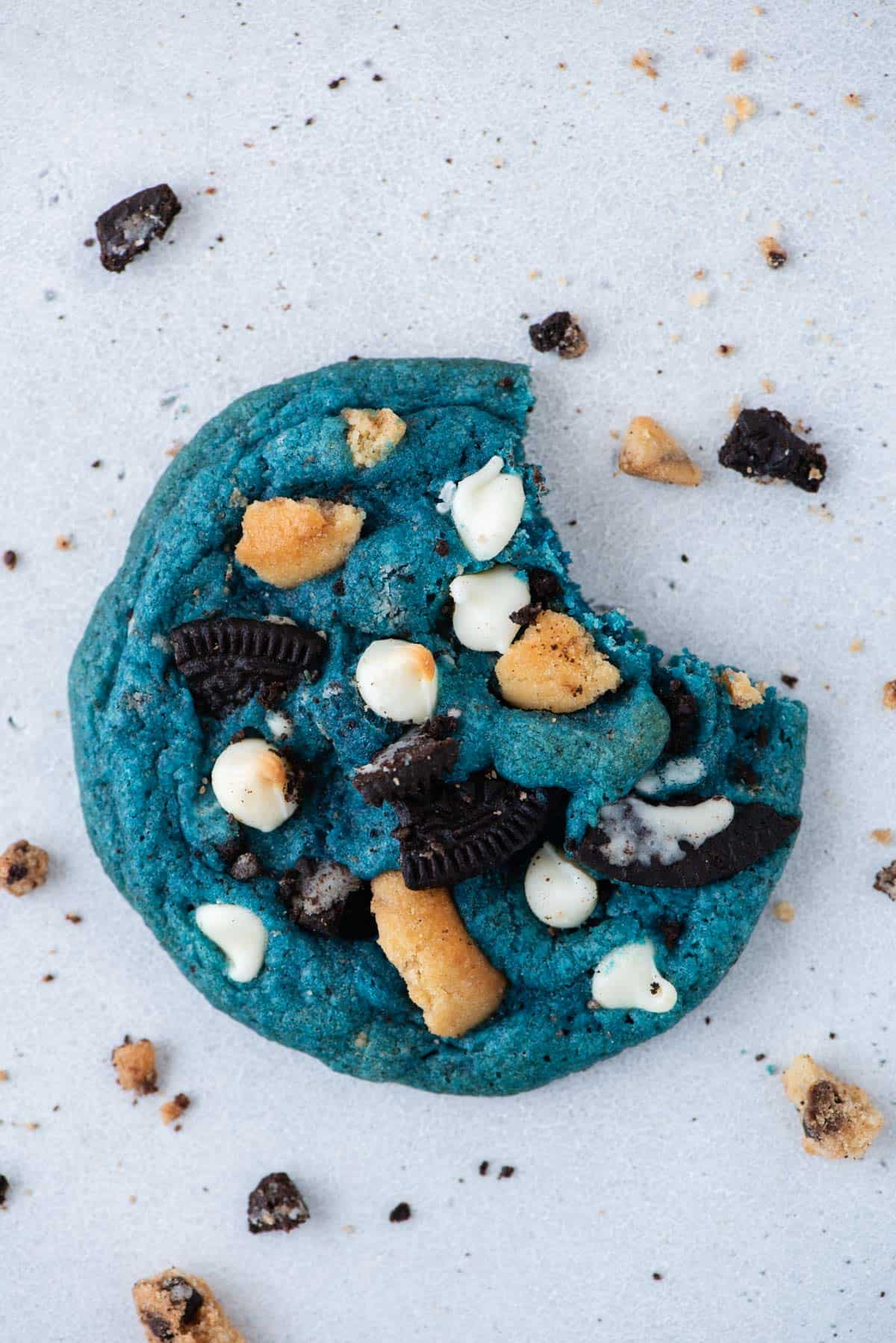 One cookie monster cookie with a bite taken out of it surrounded by cookie crumbs