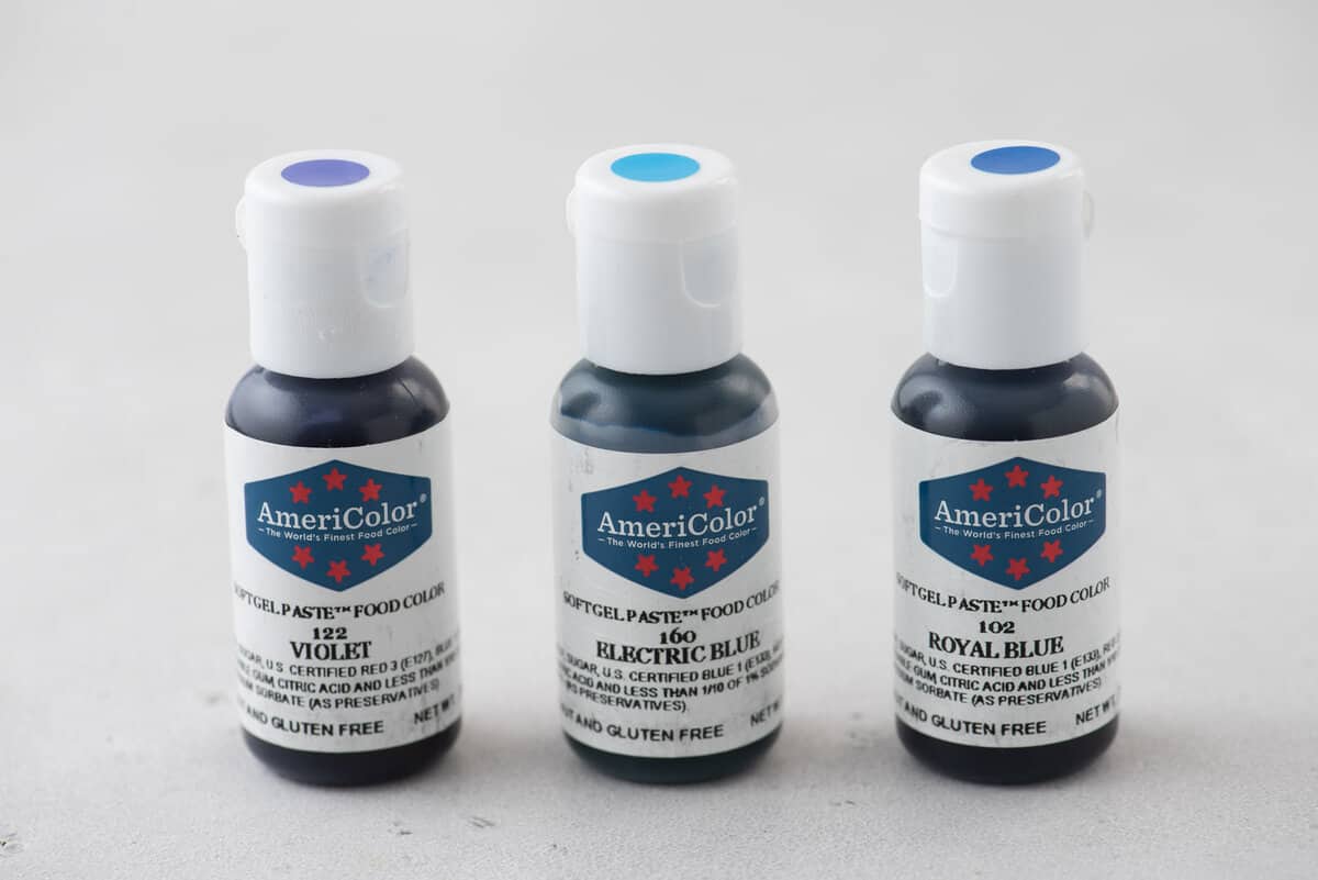 Three AmeriColor food coloring bottles in a row: violet, electric blue and royal blue