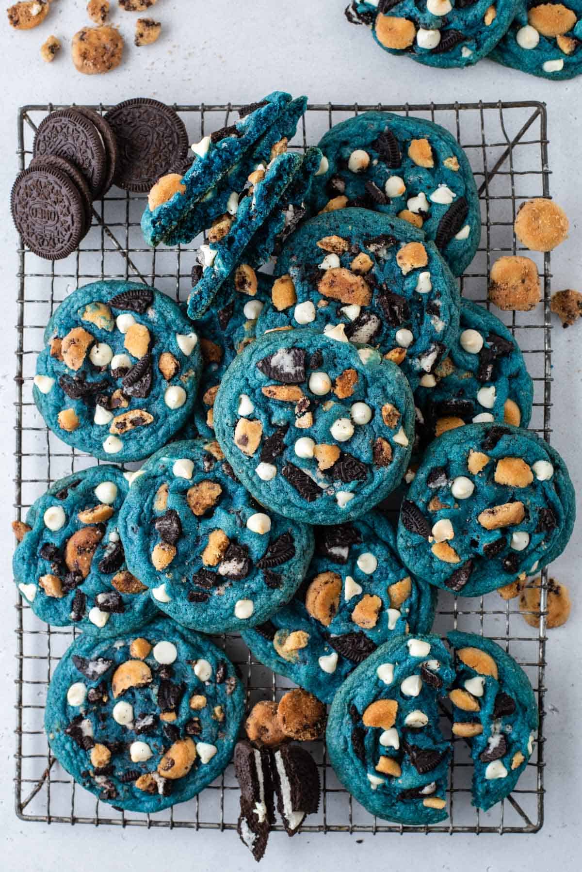 a pile of cookie monster cookies on a wire cooling rack with oreos and mini chips ahoy cookies sprinkled around