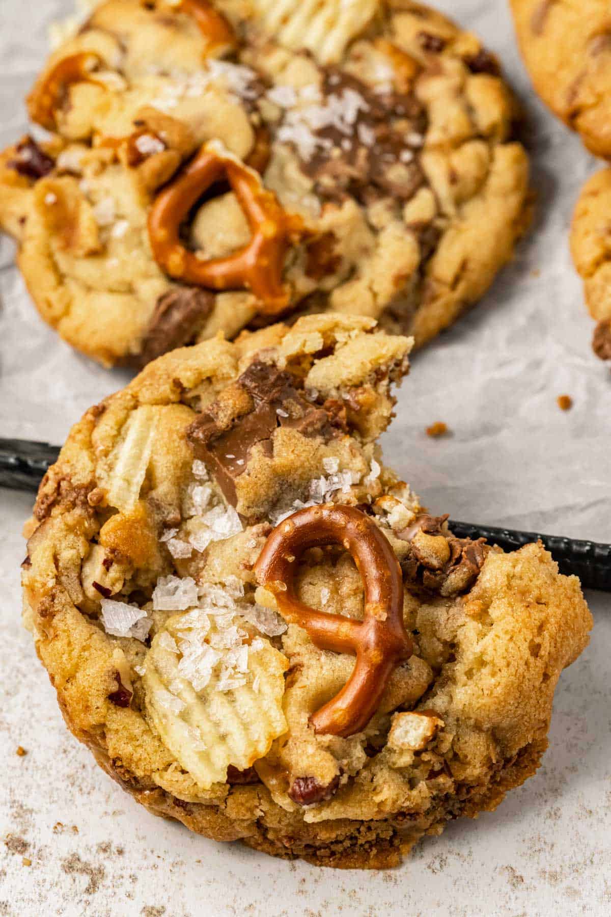close up of a kitchen sink cookie with a bite taken out, leaning on a sheet pan with more kitchen sink cookies on it