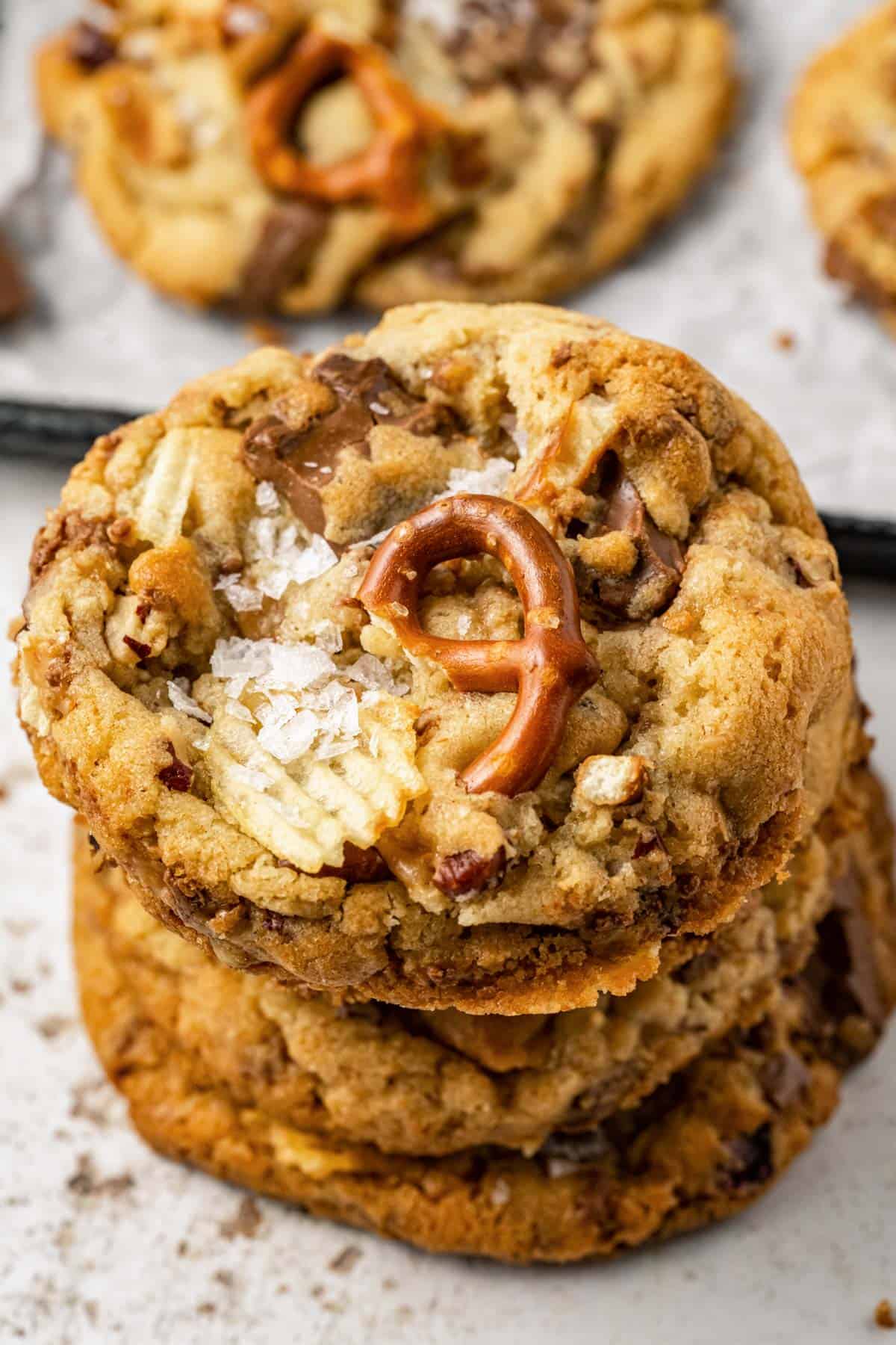 a stack of kitchen sink cookies piled up with a sheet pan behind it with more cookies on it