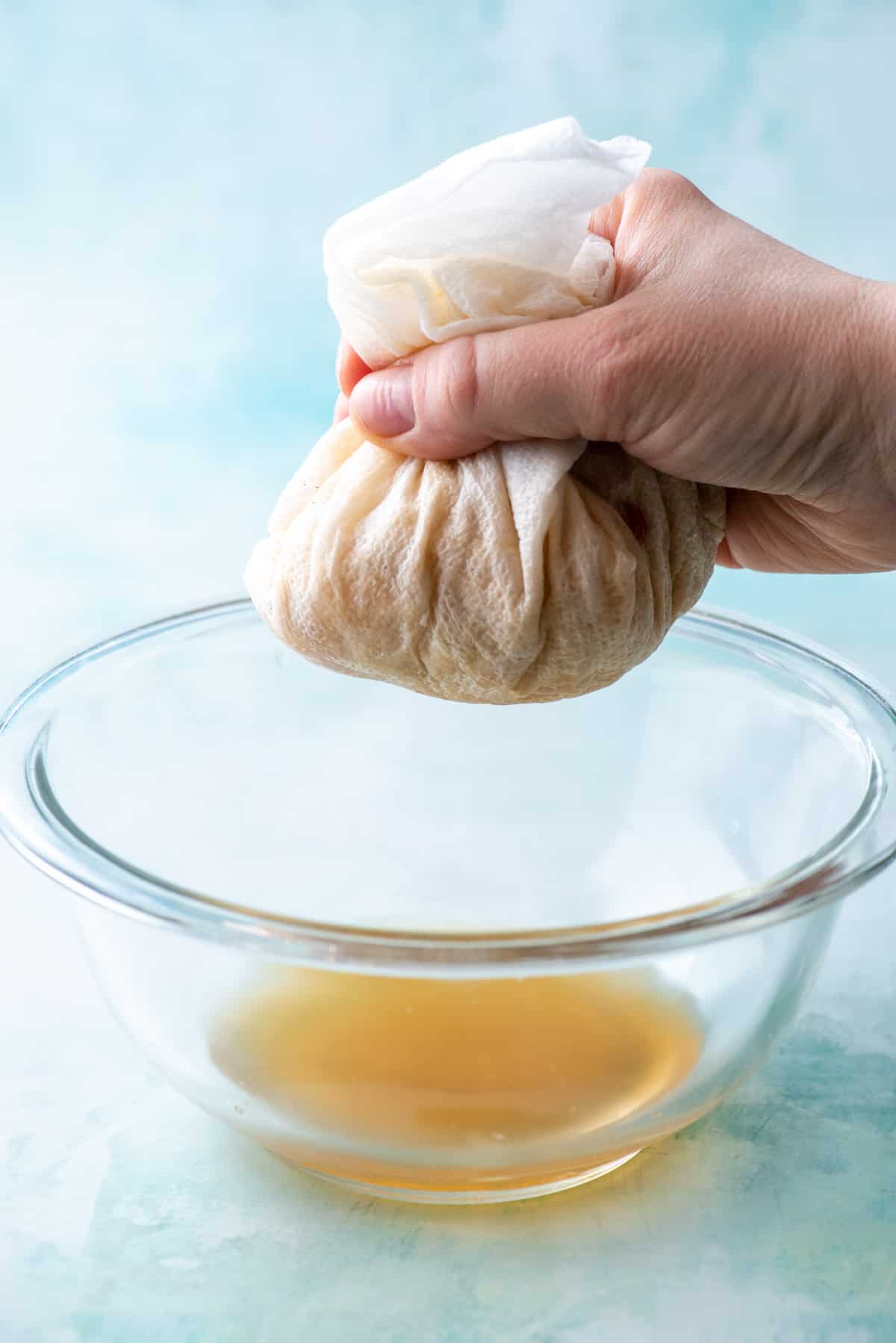 apples wrapped in paper towels being squeezed over a glass bowl to remove excess liquid