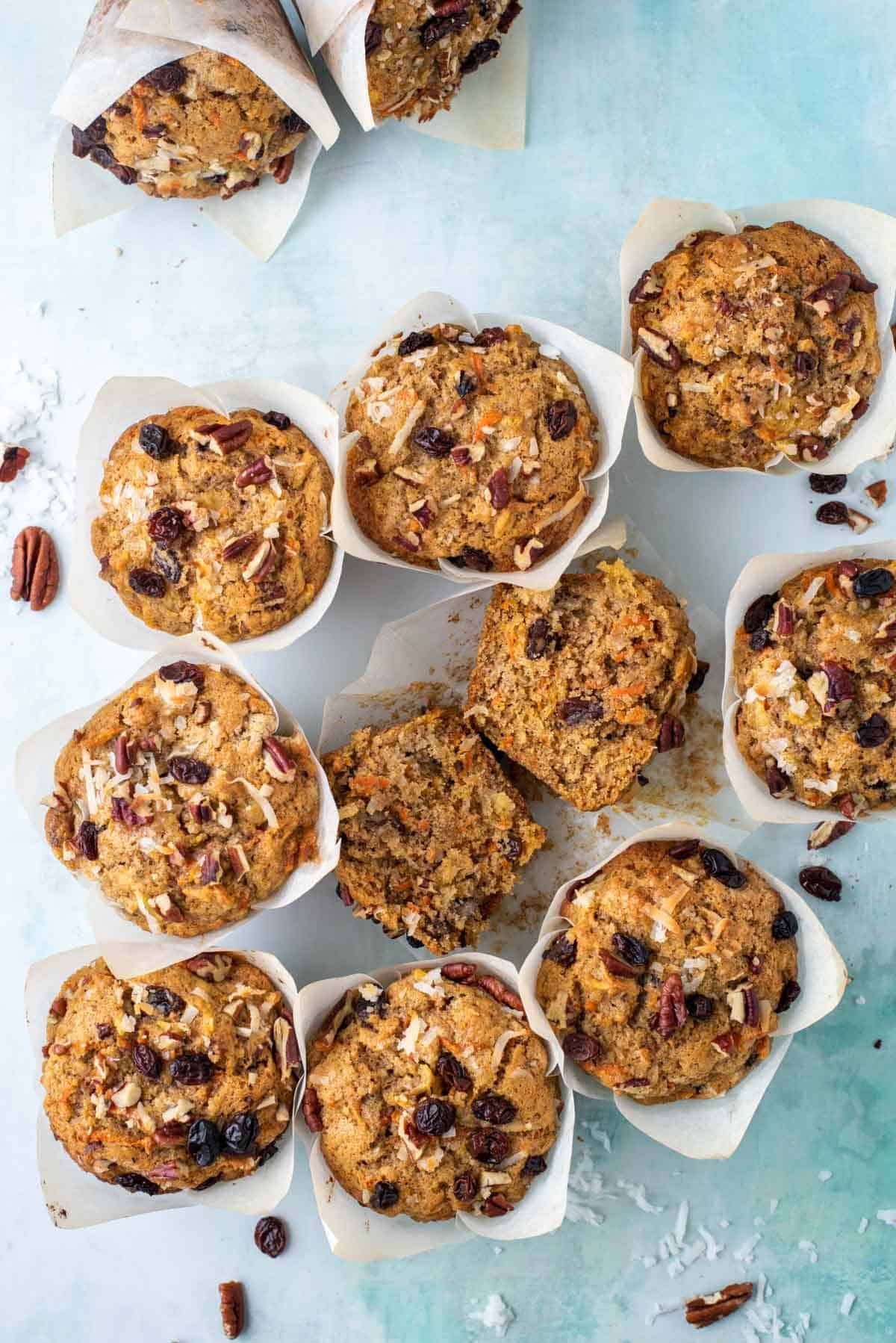 one morning glory muffin cut in half inside muffin paper surrounded by several more muffins, nuts, raisins and coconut shreds