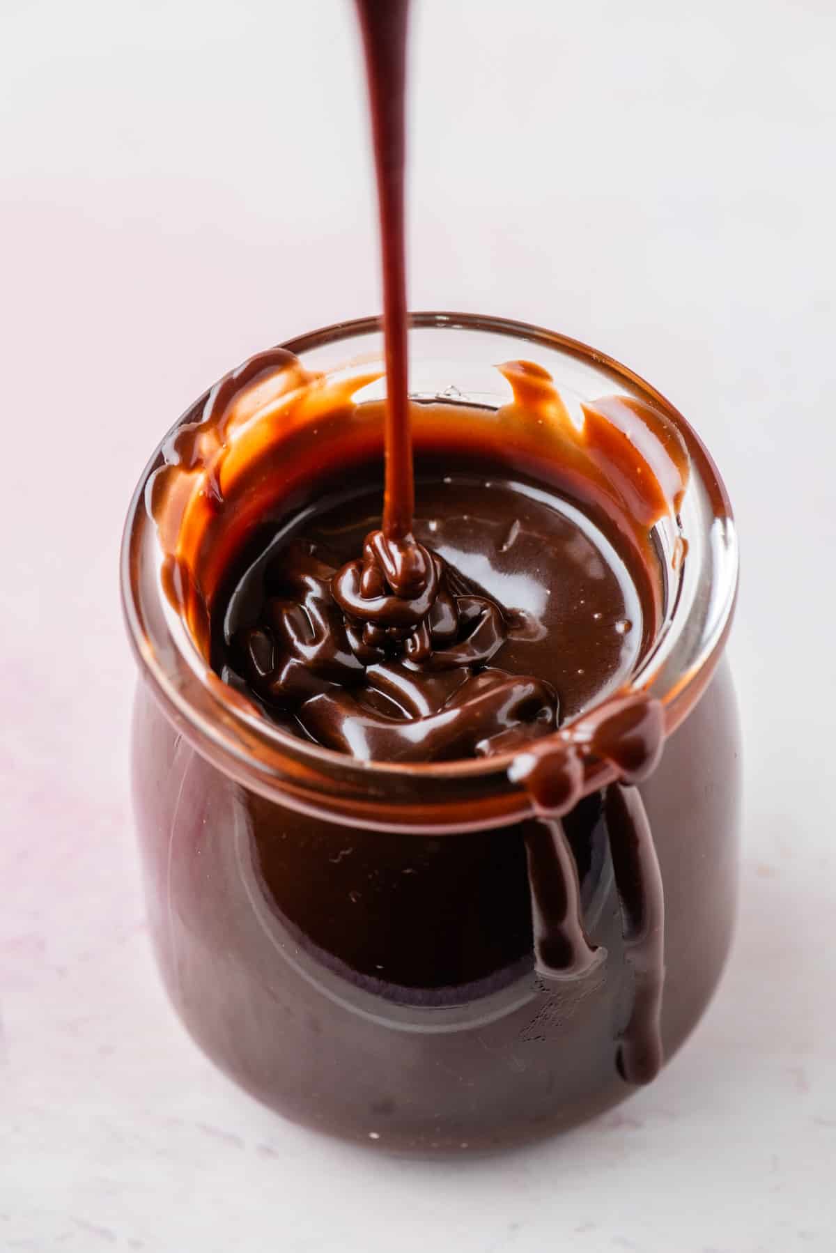 a jar of hot fudge sauce with a drizzle of sauce that is dripping down and sauce dripping down the side of the jar