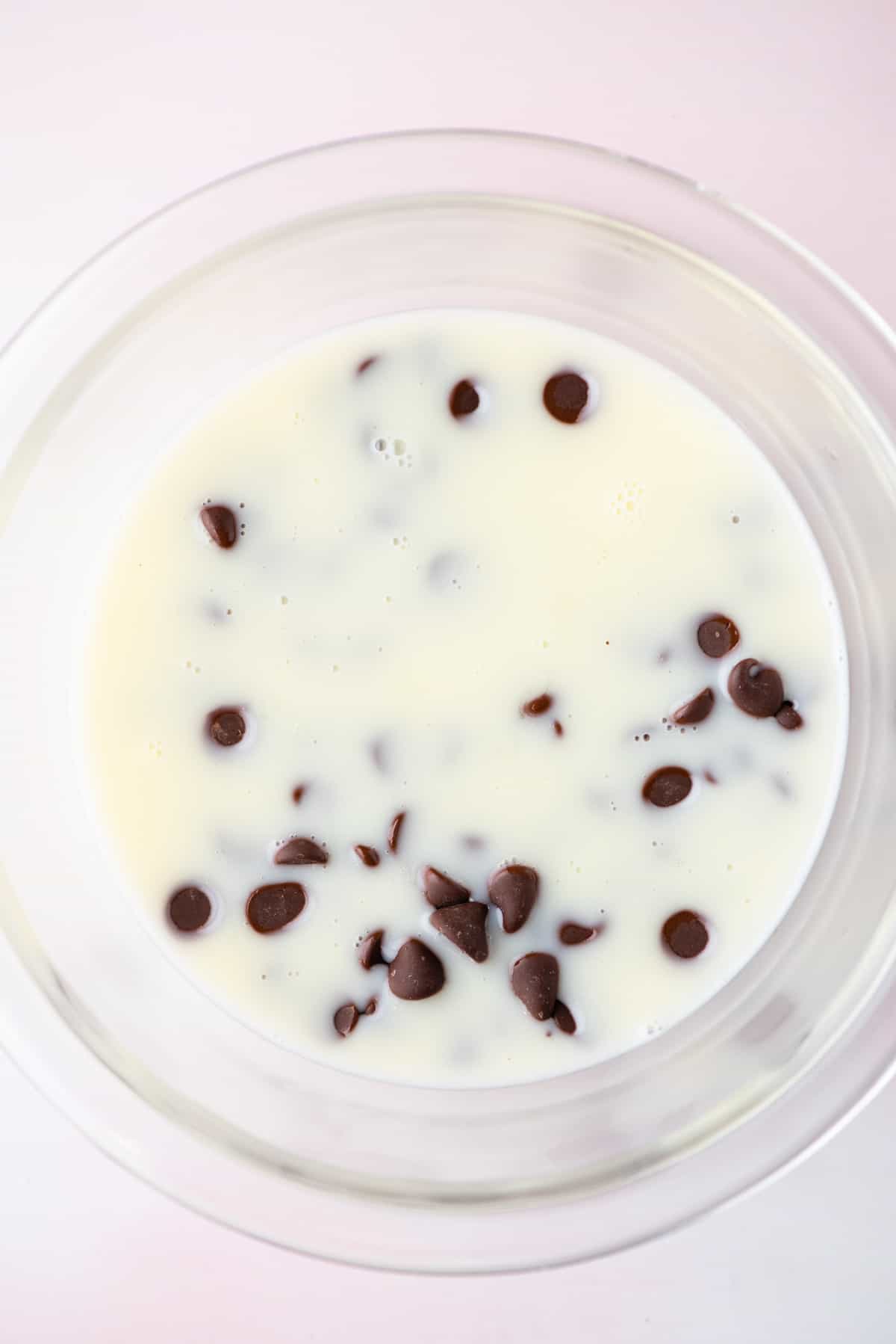 A heavy cream and sugar mixture in a glass bowl with chocolate chips