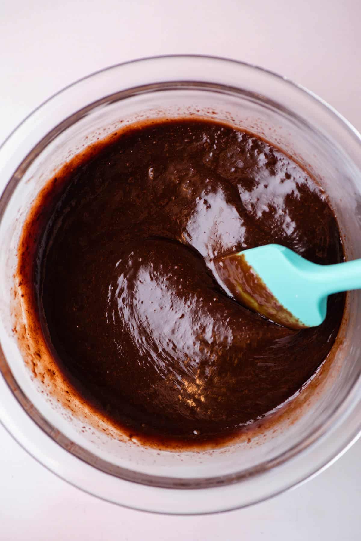 hot fudge sauce in a glass bowl that has been mixed with a teal spatula leaning in the bowl