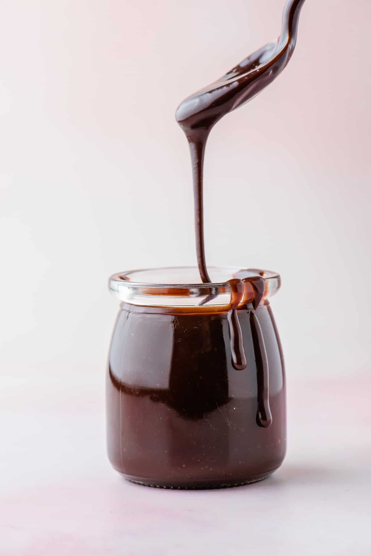 hot fudge sauce in a glass jar with a spoon showing the thick warm sauce dripping down into the jar