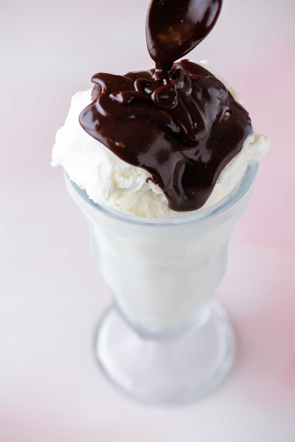 a tall glass filled with vanilla ice cream being topped with hot fudge sauce