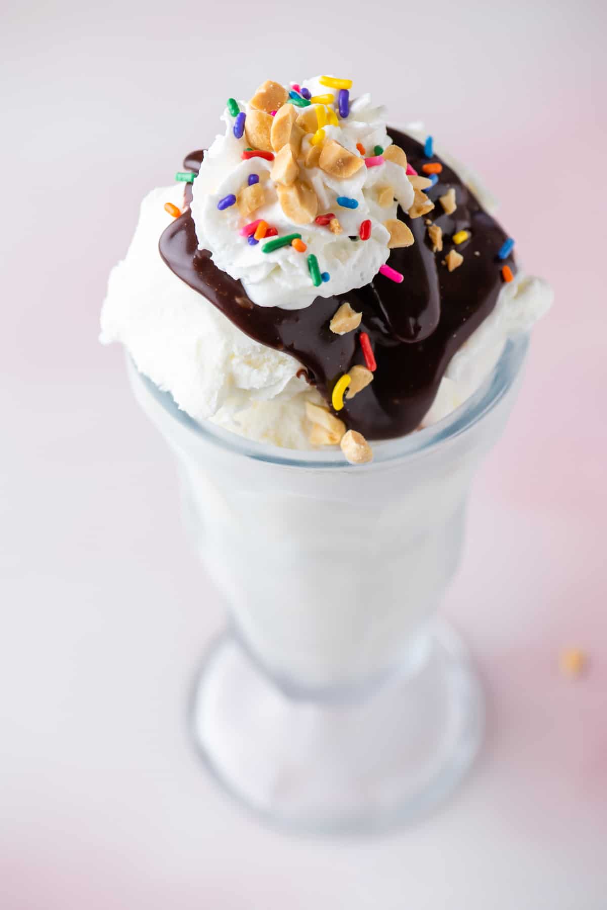 a hot fudge sundae in a tall glass topped with sprinkles, peanuts and cool whip