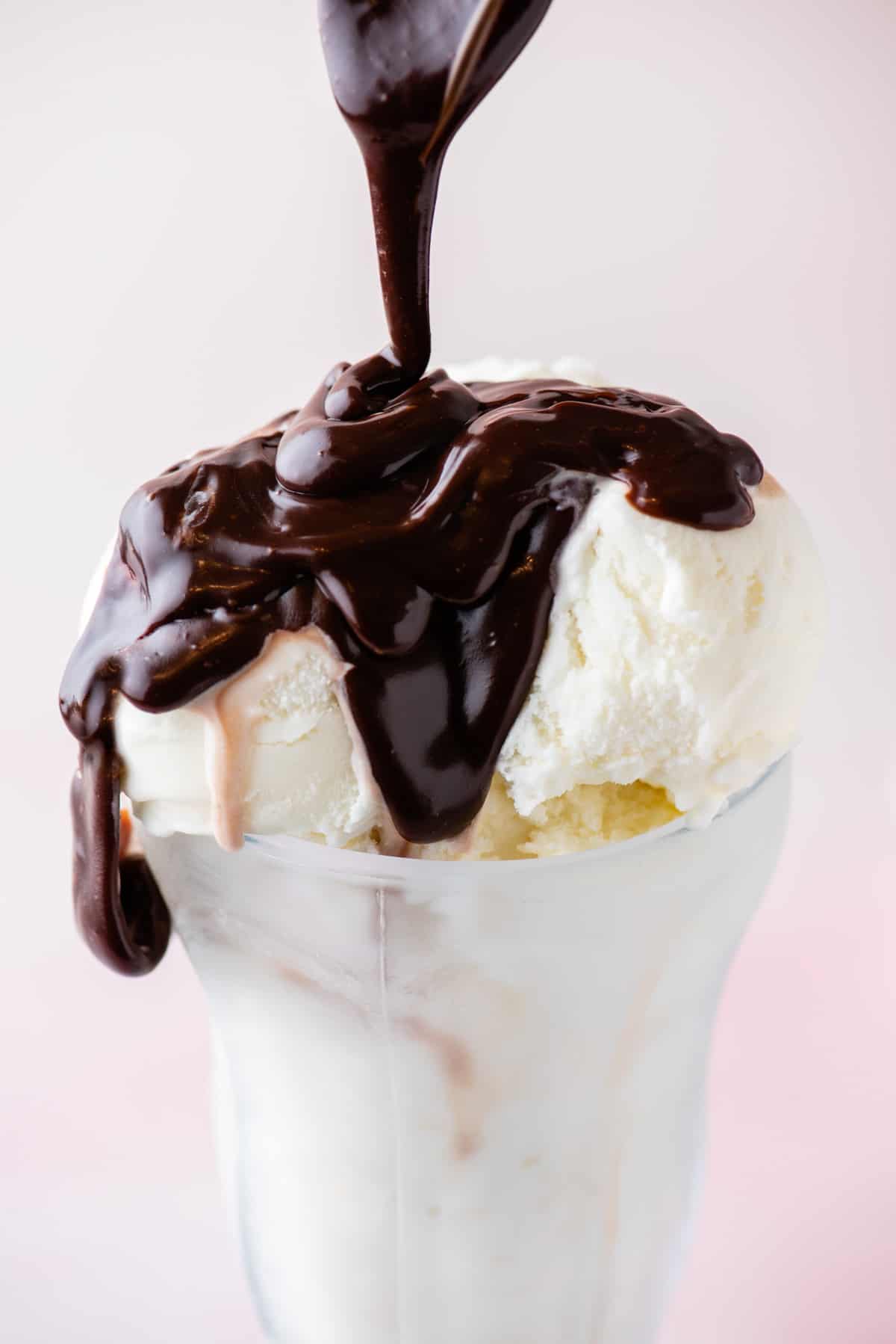 vanilla ice cream in a tall glass being topped with hot fudge sauce