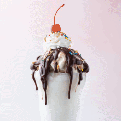 a hot fudge sundae topped with peanuts, sprinkles and a cherry on top against a pink background