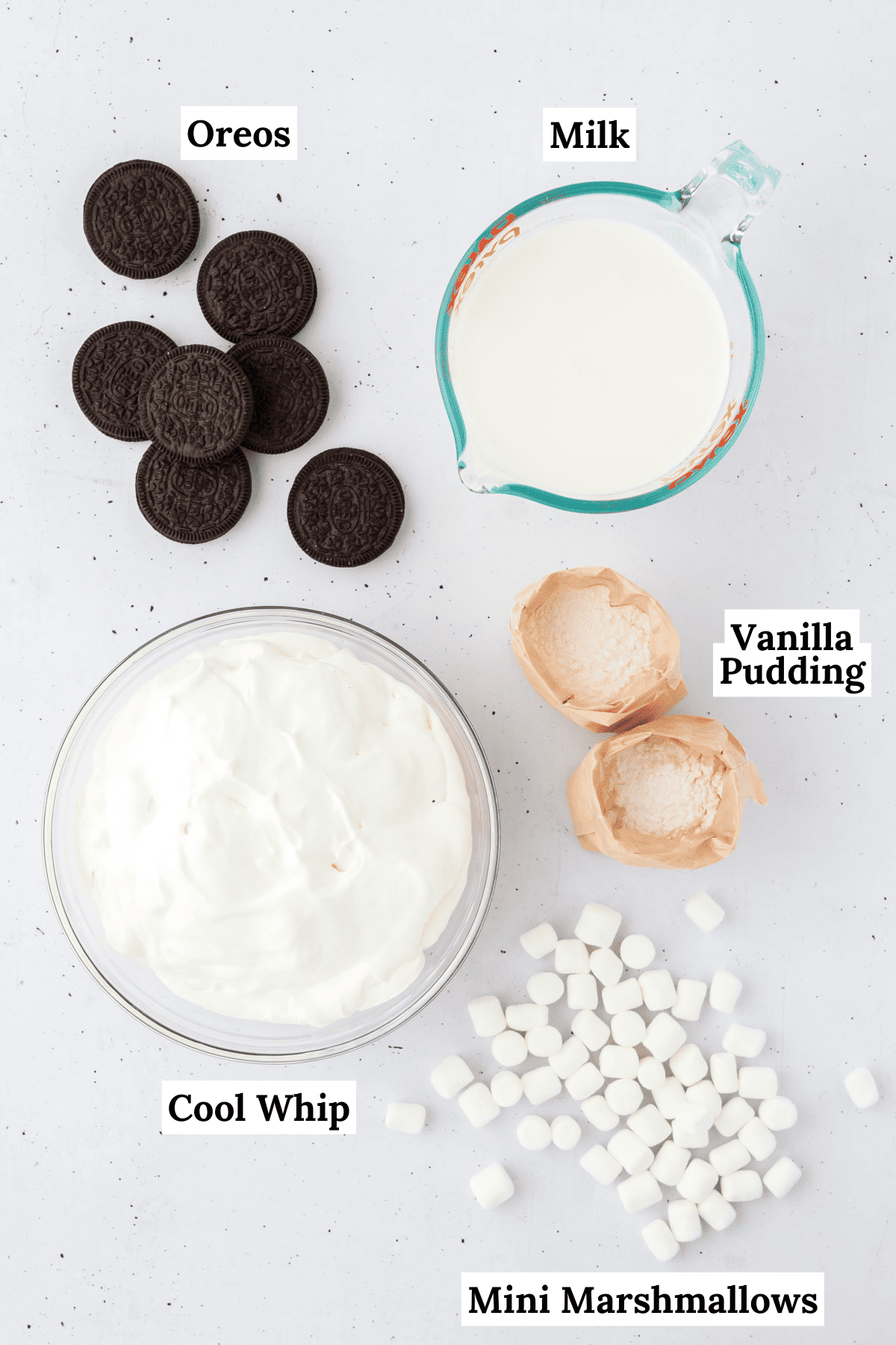 ingredients for oreo fluff laid out on a white surface including vanilla pudding mix, milk, cool whip, oreos, and mini marshmallows