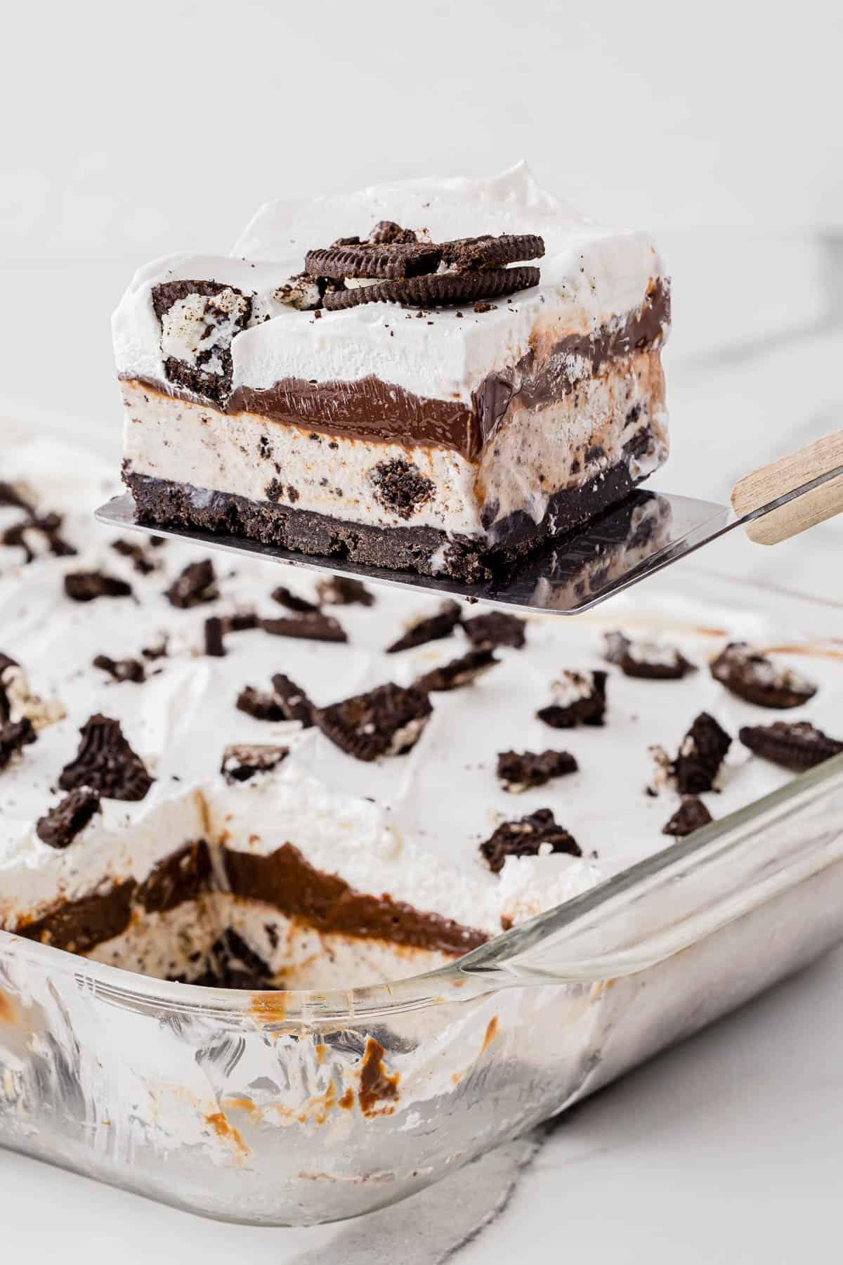 a slice of oreo ice cream cake being lifted out of a dish with a spatula