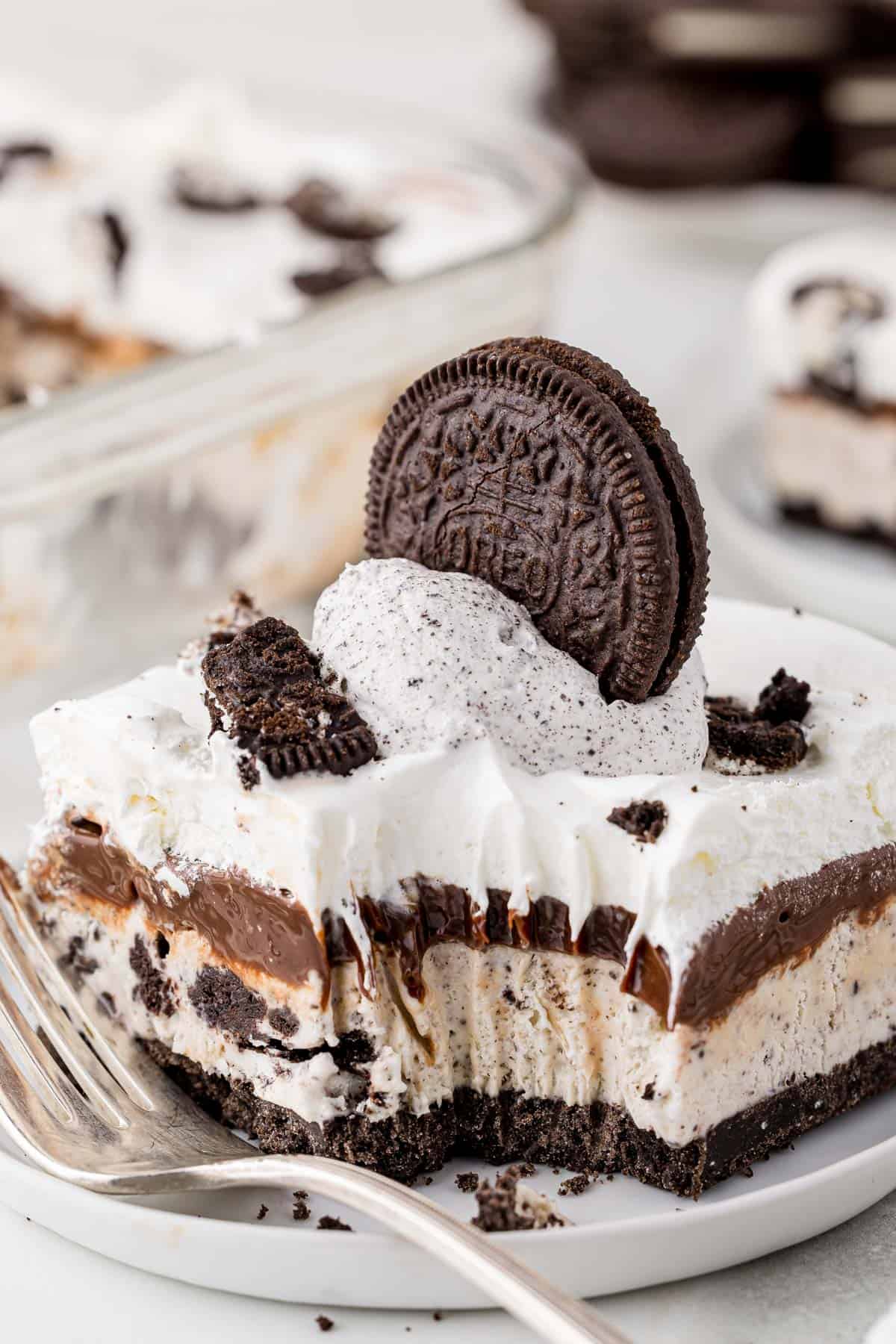 a slice of oreo ice cream cake on a white plate with a bite taken out and a fork laying on the plate 