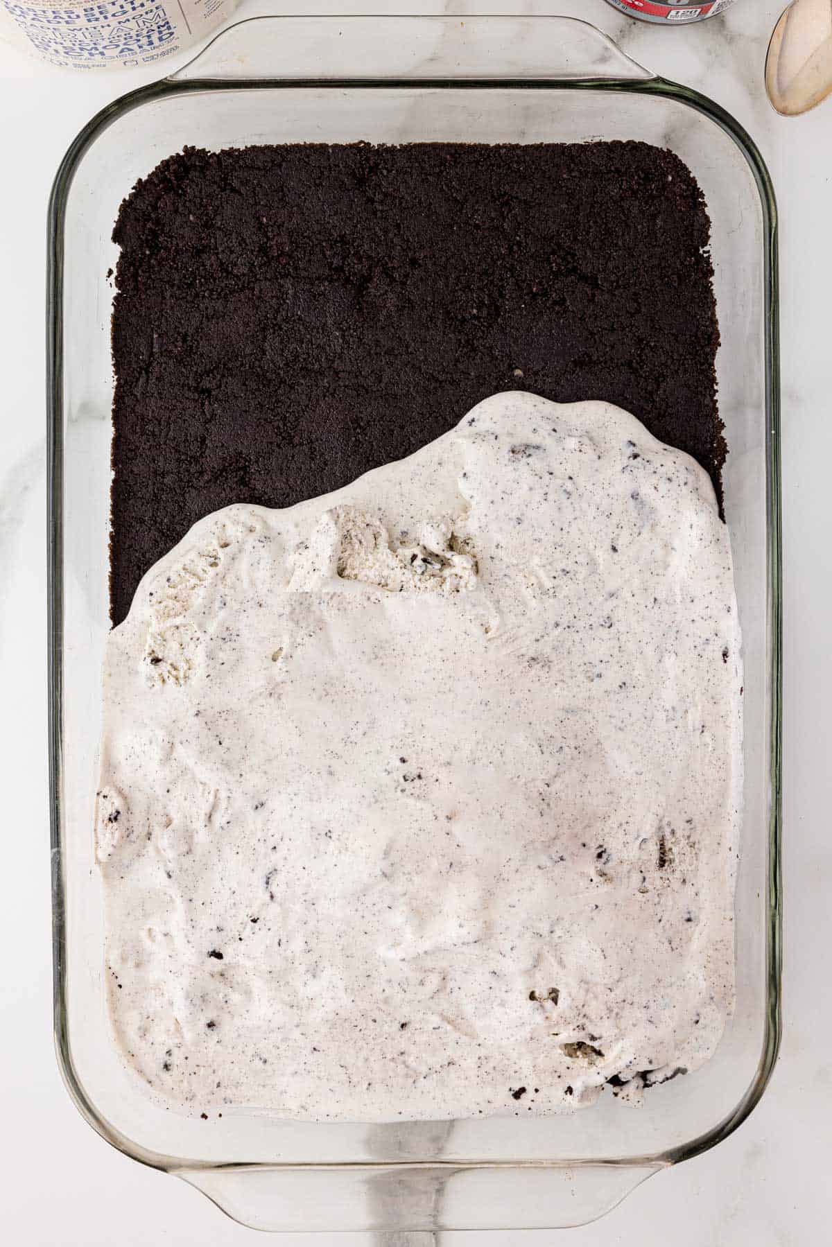 layers of oreo ice cream cake being added to a baking dish with oreo crust on the bottom and cookies and cream ice cream half spread on top