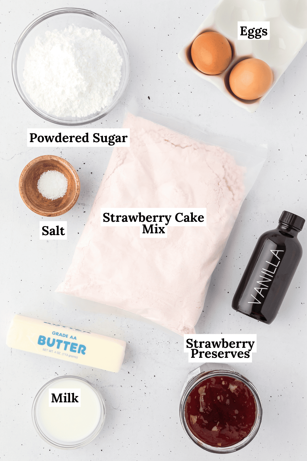 The ingredients for strawberry brownies laid out on a counter including eggs, powdered sugar, salt, strawberry cake mix, vanilla, strawberry preserves, butter and milk