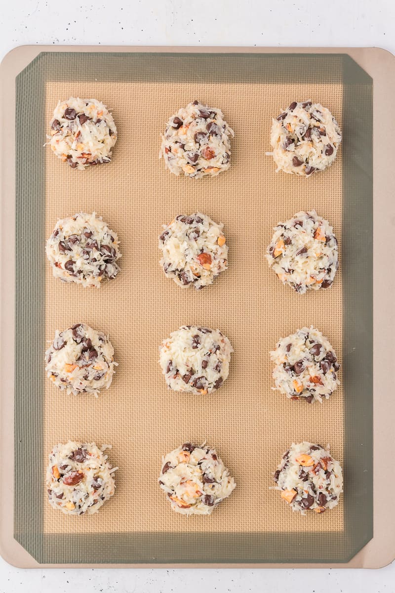 almond joy cookie balls arranged in rows of 3 on a silicone baking mat on a cooking sheet