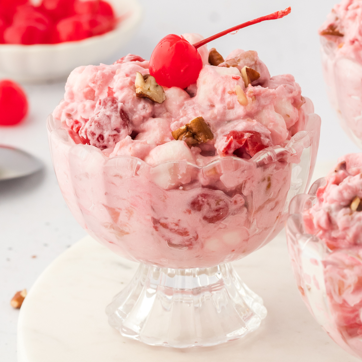 cherry fluff in a glass bowl topped with a maraschino cherry