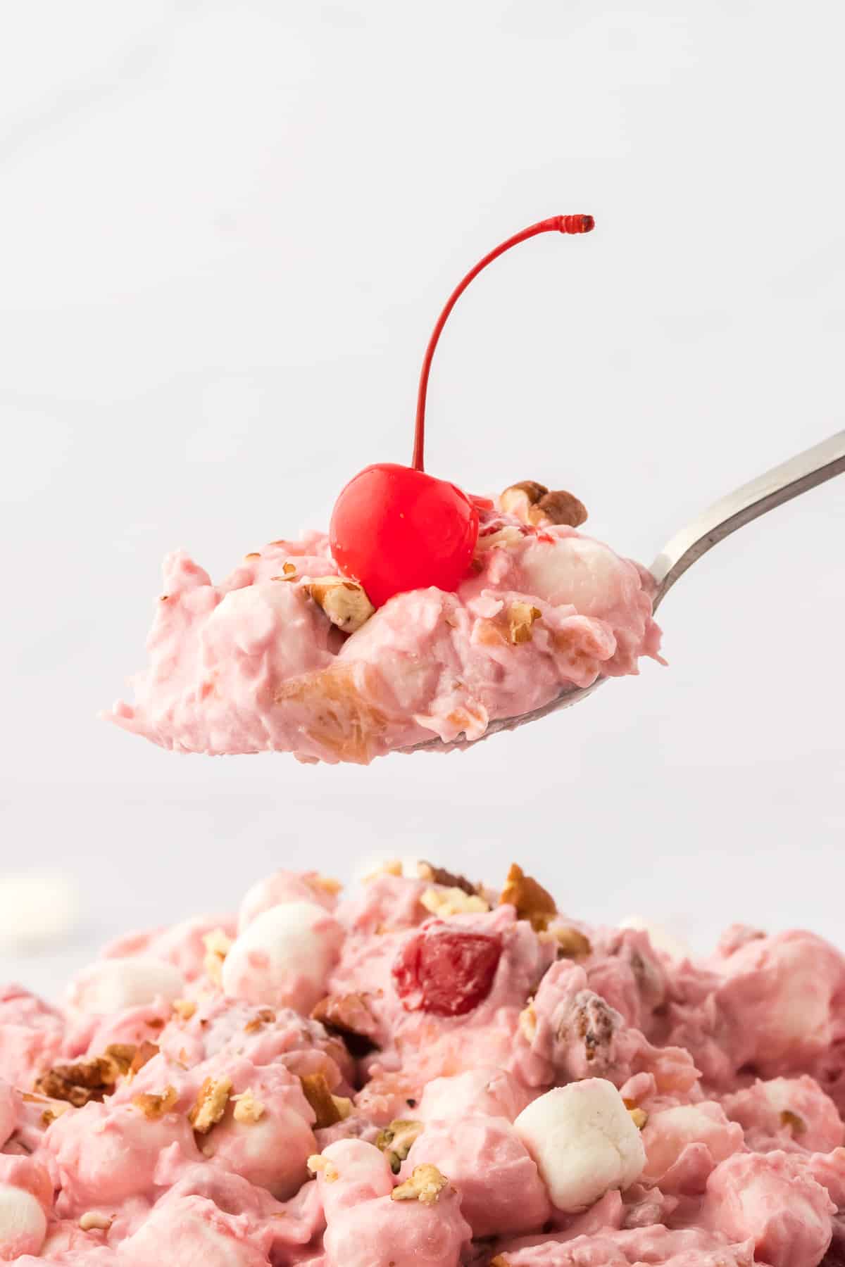 a spoon full of cherry fluff topped with a maraschino cherry held above more cherry fluff salad