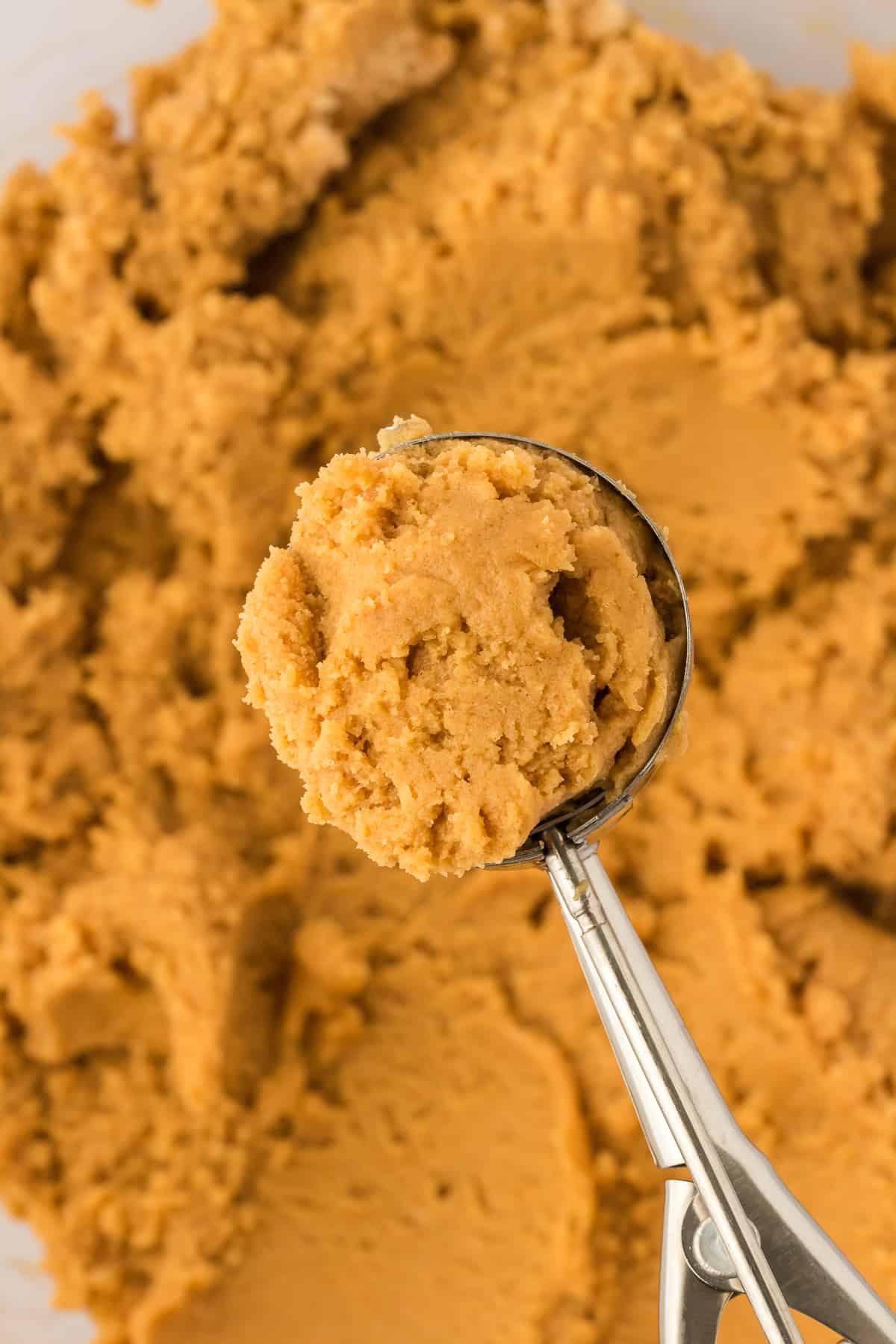 a cookie scoop full of gluten free peanut butter cookie dough over of a bowl of cookie dough