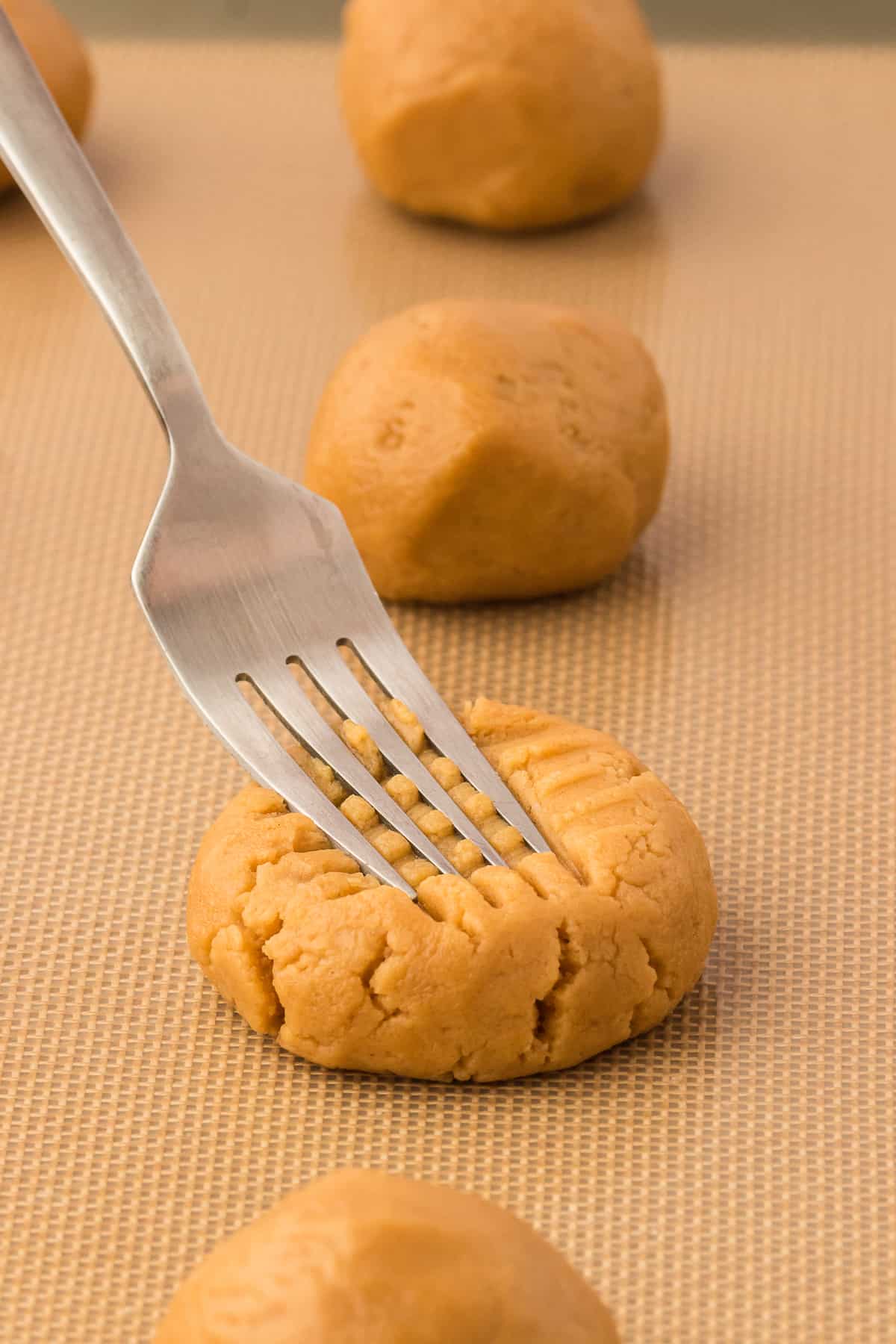 a fork creating a cross hatch pattern on gluten free peanut butter cookie dough balls on a baking sheet