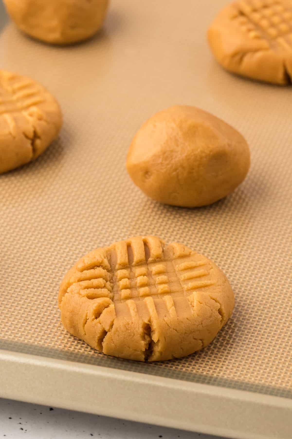 gluten free peanut butter cookie dough balls on a lined baking sheet, some pressed down into a cross hatch pattern and some still in ball form