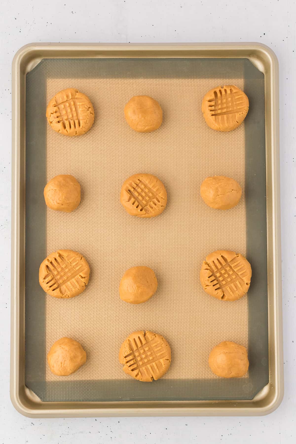 gluten free peanut butter cookie dough balls on a lined baking sheet, some pressed down into a cross hatch pattern and some still in ball form