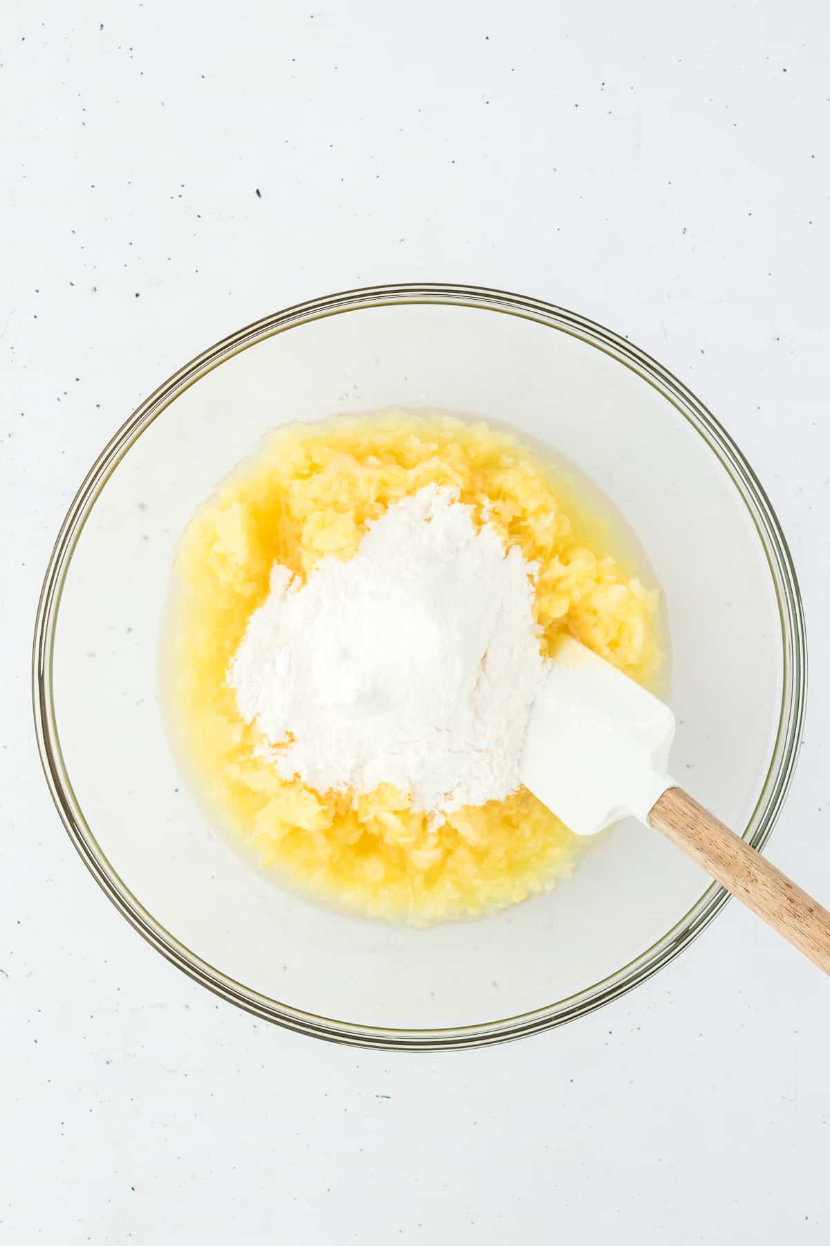 crushed pineapple and vanilla pudding mix in a clear glass bowl with a spatula in it