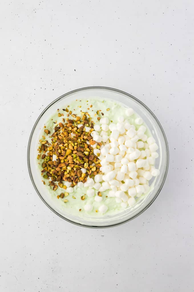 ingredients for pistachio salad with pistachios and marshmallows on top, not mixed in yet, in a glass bowl