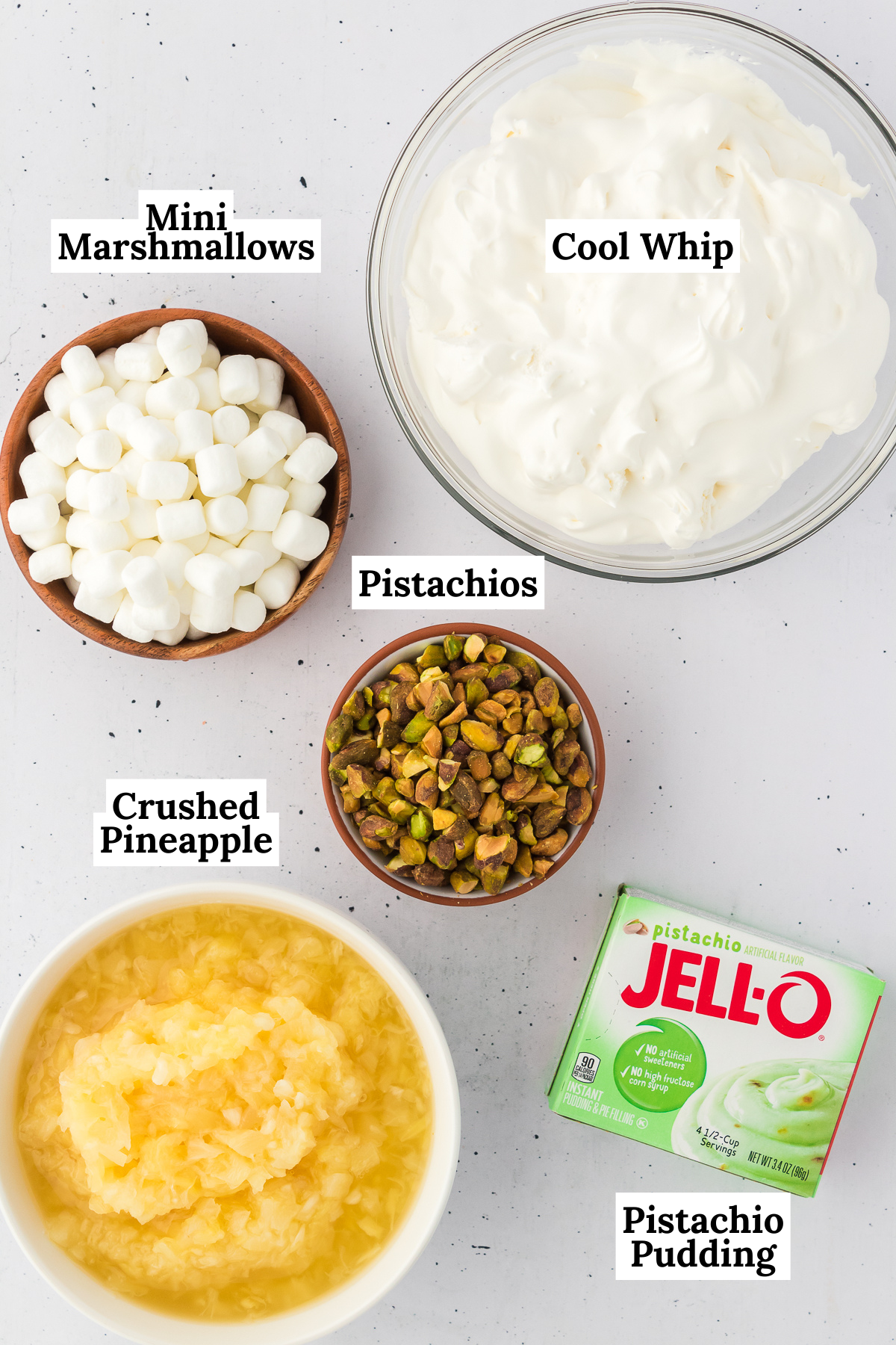 the ingredients for pistachio salad including pistachio pudding mix, crushed pineapple, cool whip, mini marshmallows, and chopped nuts