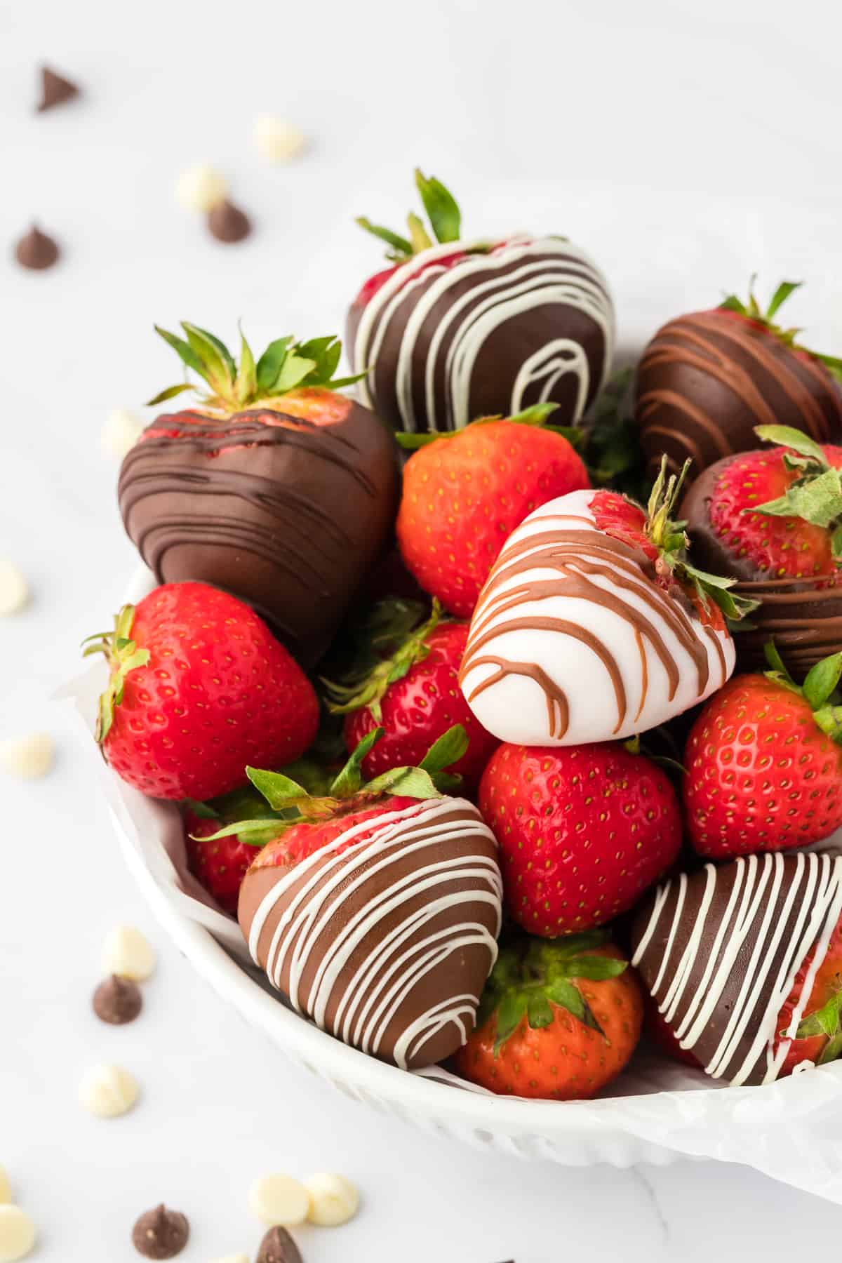 a white bowl full of chocolate covered strawberries and fresh strawberries surrounded by white and milk chocolate chips