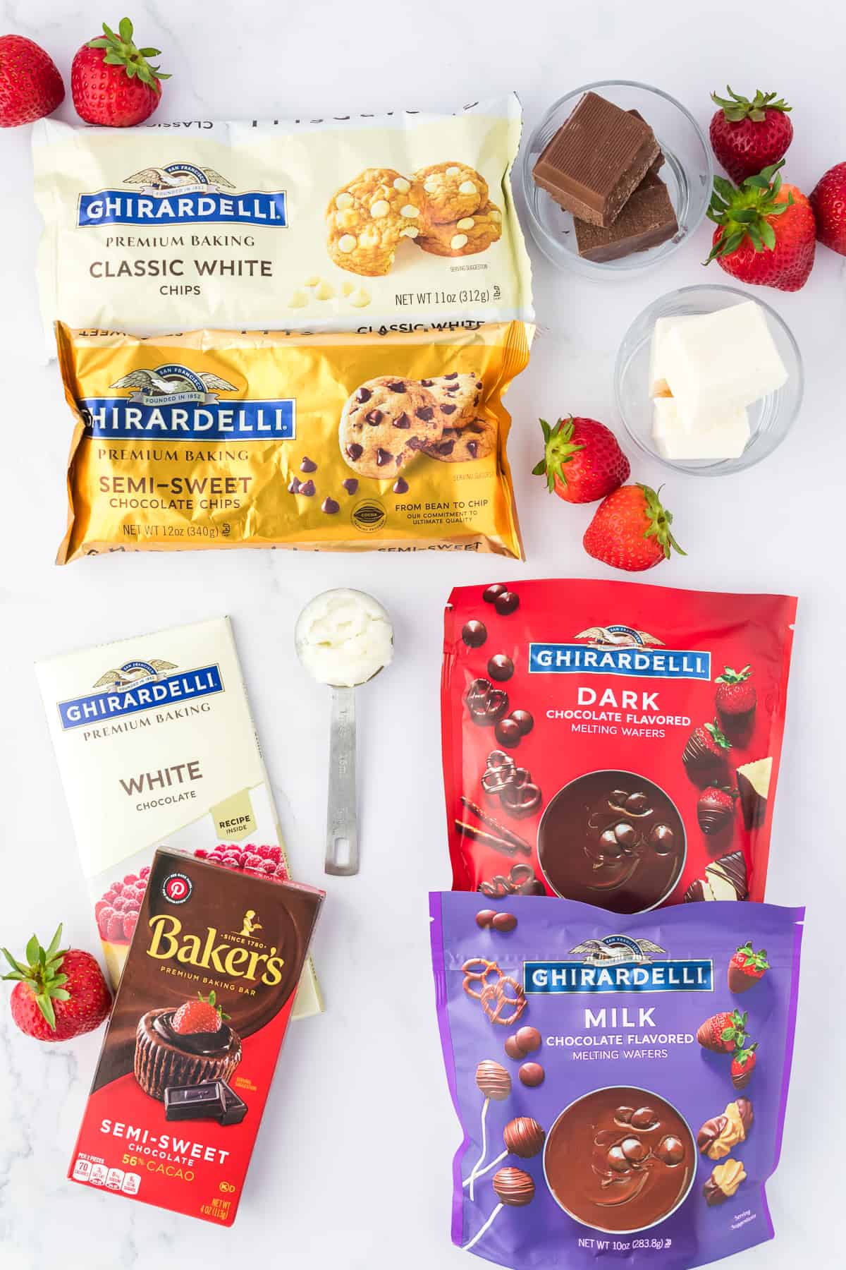 Ingredients for chocolate covered strawberries including fresh strawberries, a bag of ghiradelli classic white chips, ghiradelli semi sweet chocolate chips, white chocolate bar, semi-sweet chocolate, dark chocolate melting wafers and milk chocolate melting wafers, and coconut oil