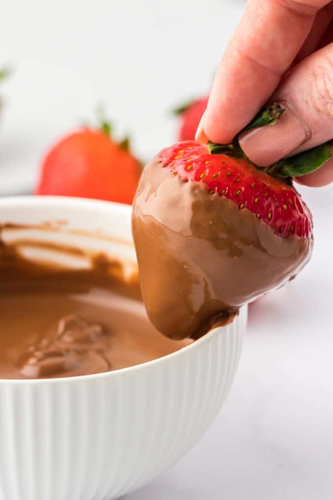 A strawberry that has been dipped into a bowl of chocolate being run along the inner edge of the bowl to remove excess chocolate